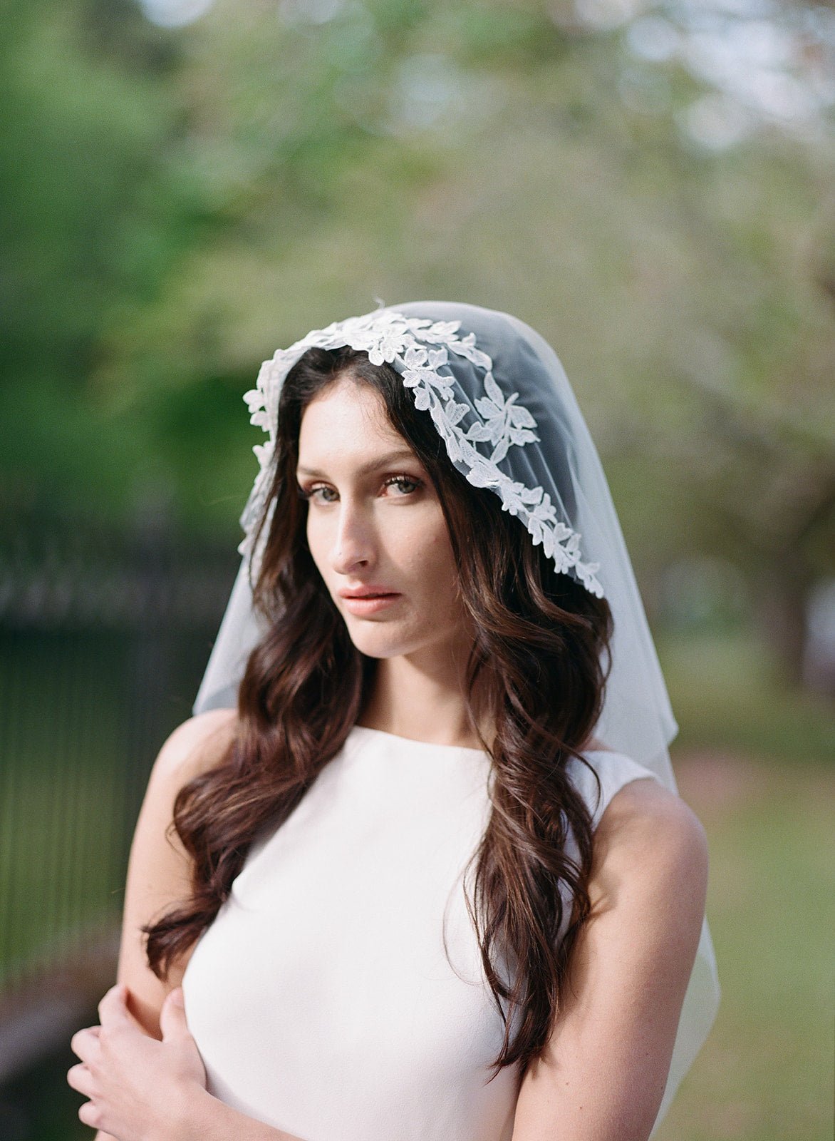 A bride looks onwards, her head haloed by her floral lace wedding veil.