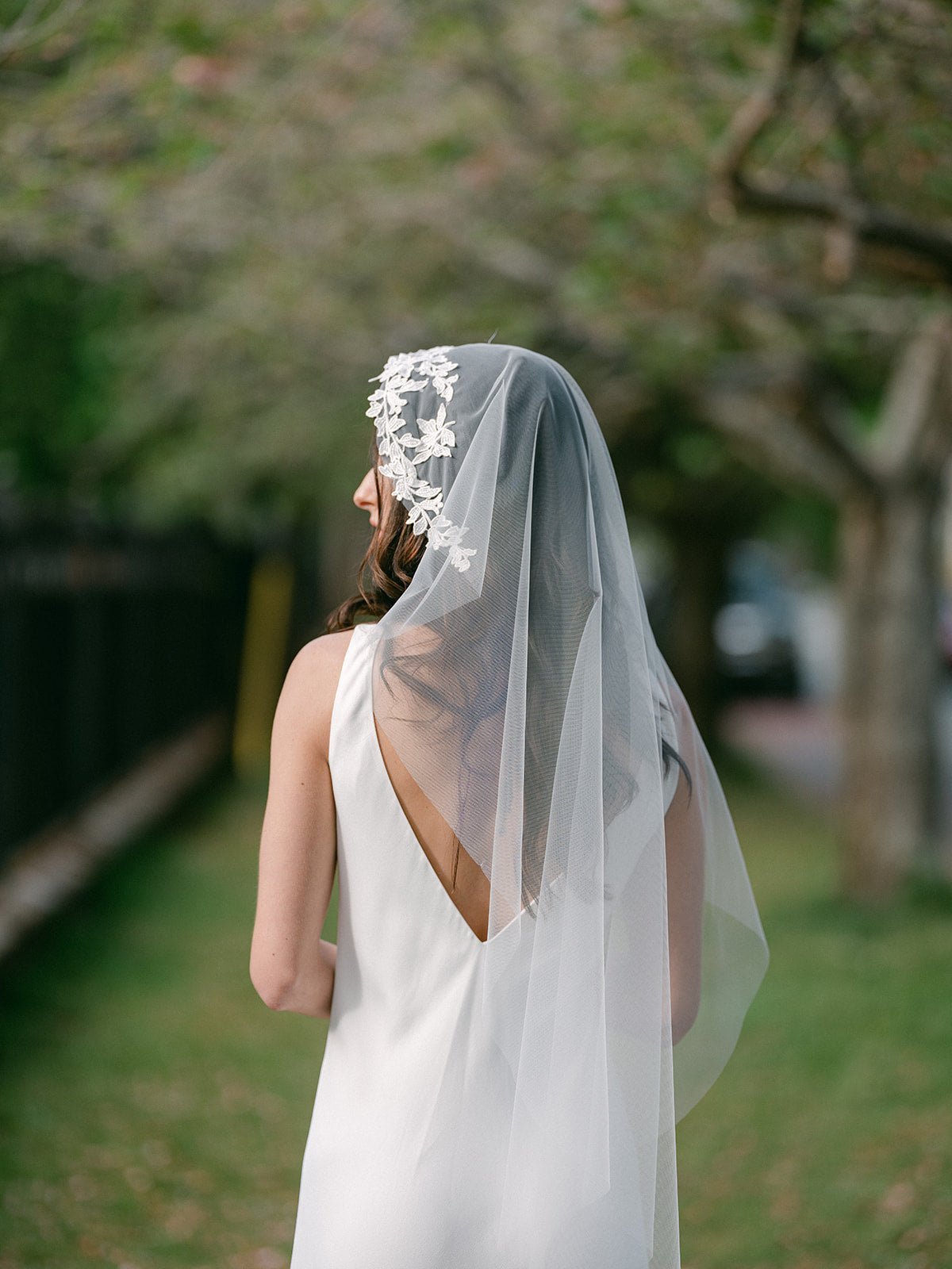 A bride looks aside while wearing a lacey topped tulle wedding veil. 