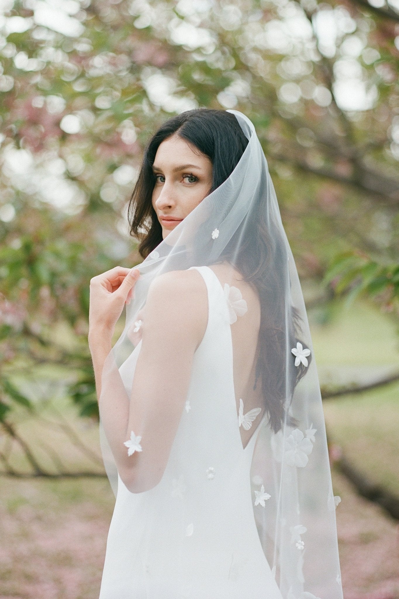 A coy bride hides some of her face with her flower blossom embroidered veil. 