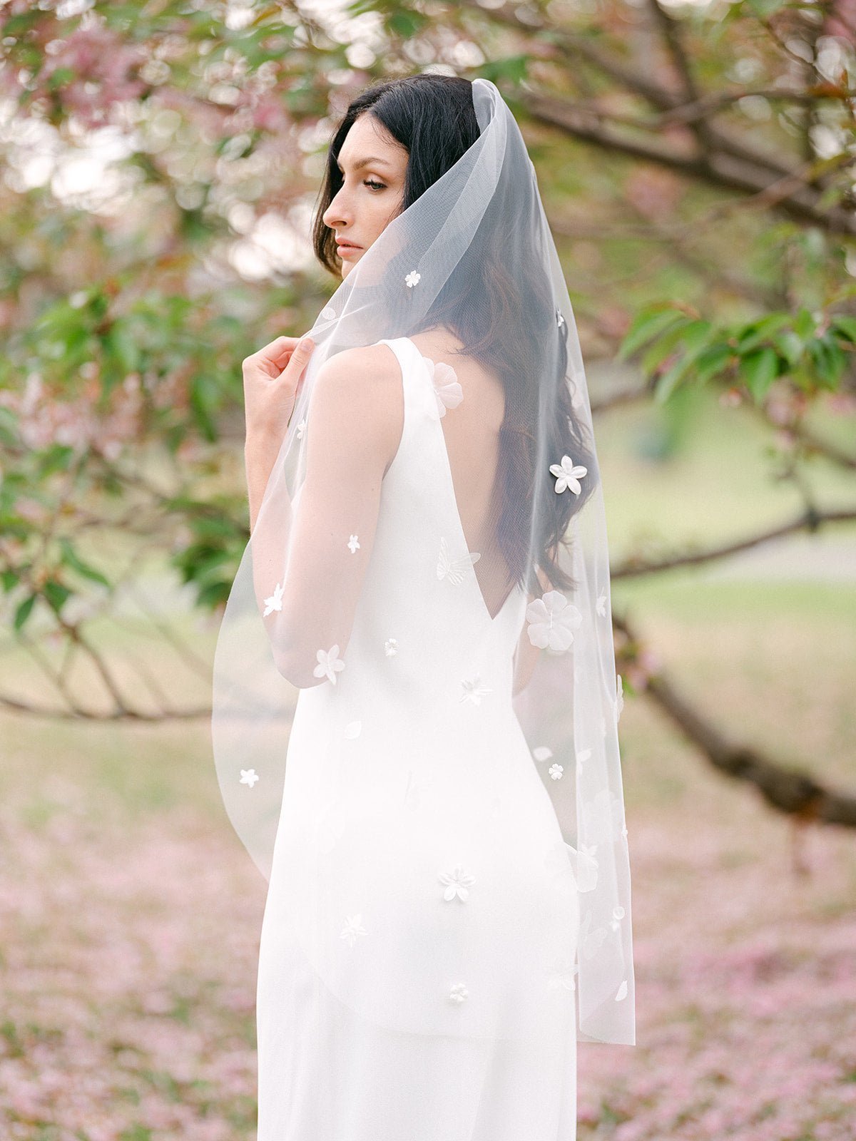 A thoughtful bride hides some of her face with her flower blossom embroidered veil. 