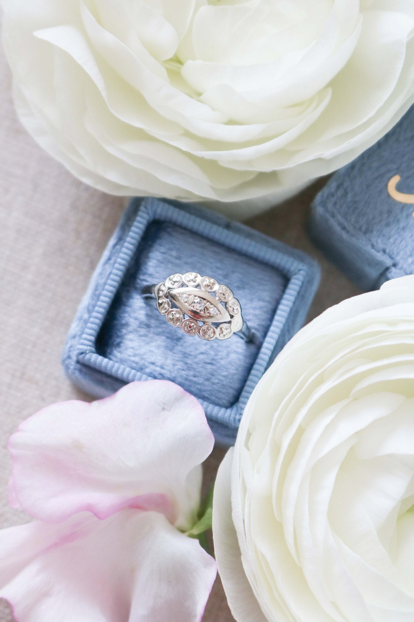 A Faye 14ct Gold Art Deco Diamond Engagement Ring circa 1920s in a ring box surrounded by white roses. 