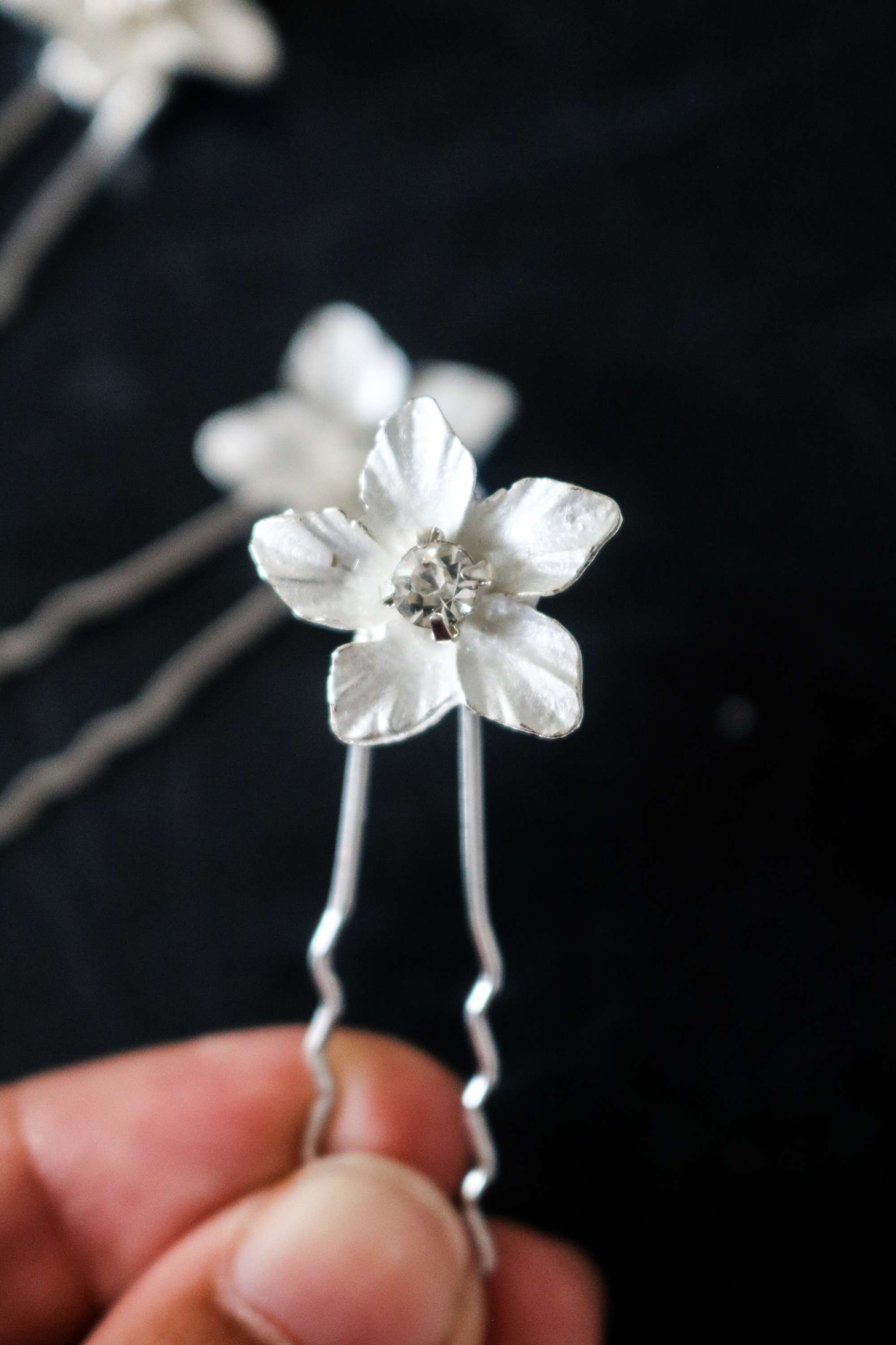 A close up of a silver crystal flower bridal hairpin being held. 