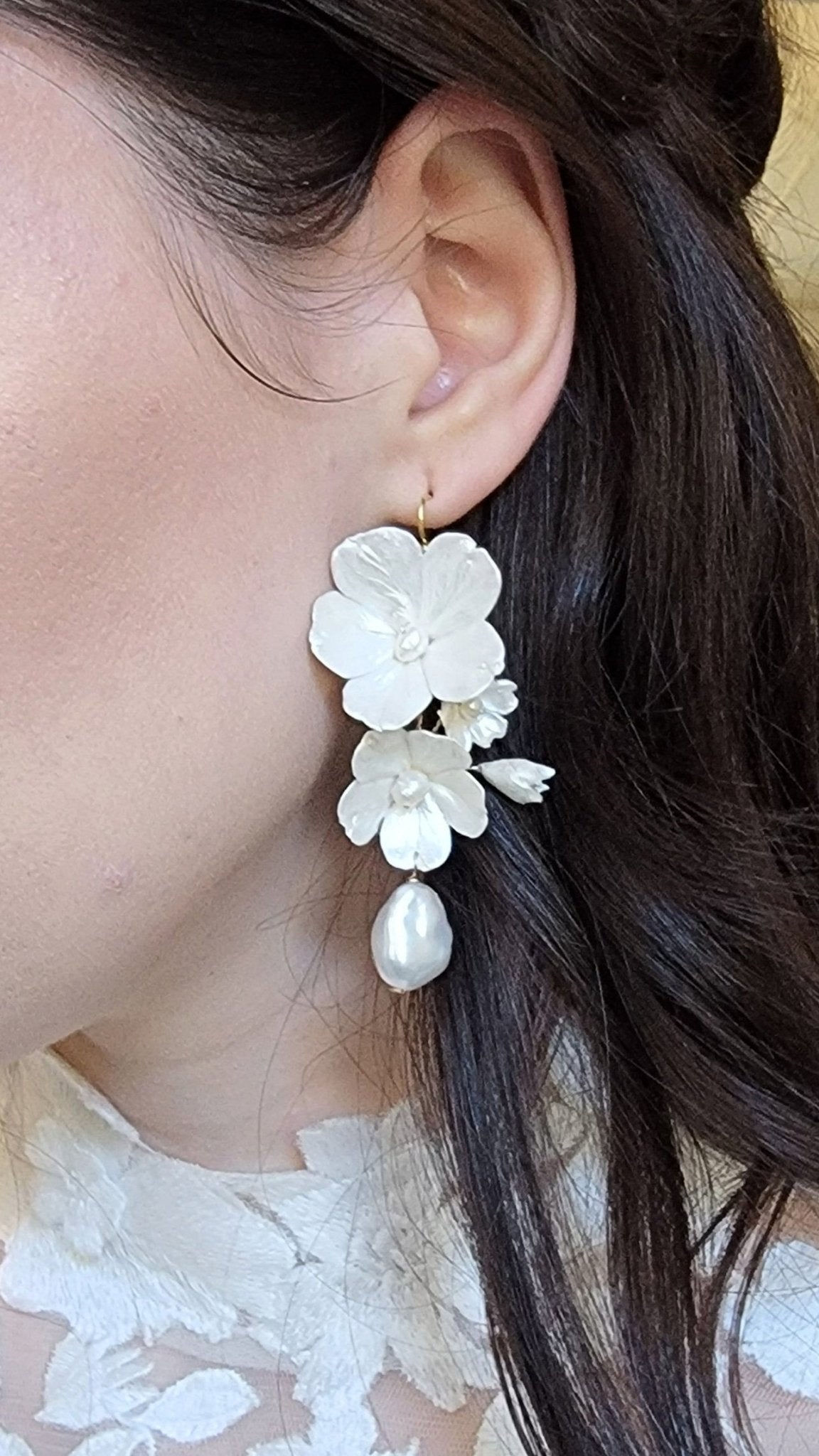 Golden enamel clay flower bridal earrings with baroque freshwater pearls hanging from an ear. 