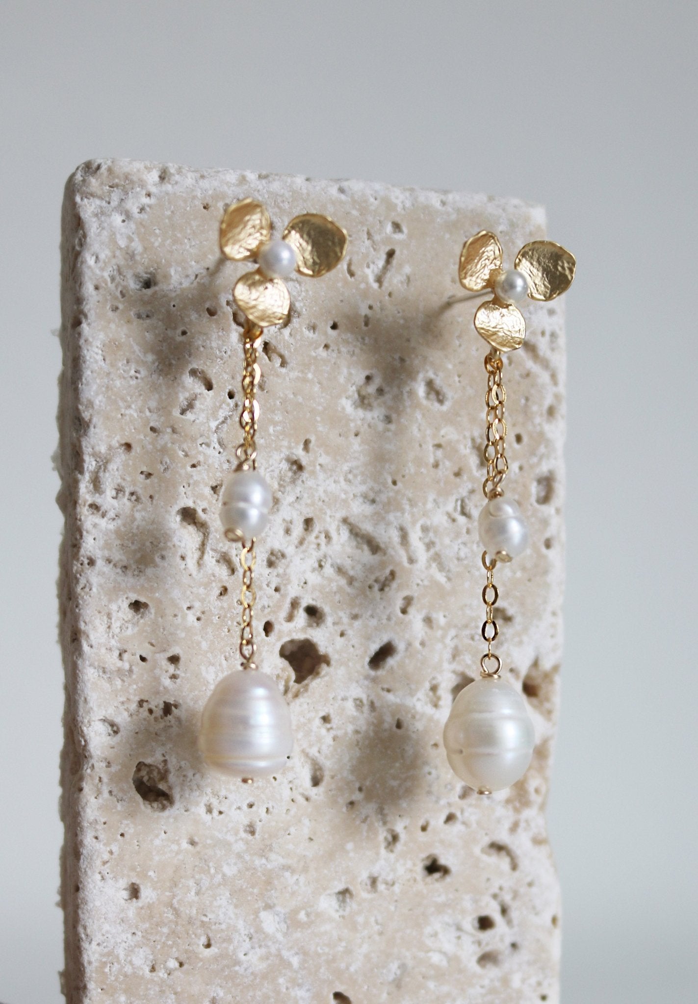 A pair of golden wedding ready pearl earrings with flowers are set in a stone block. 