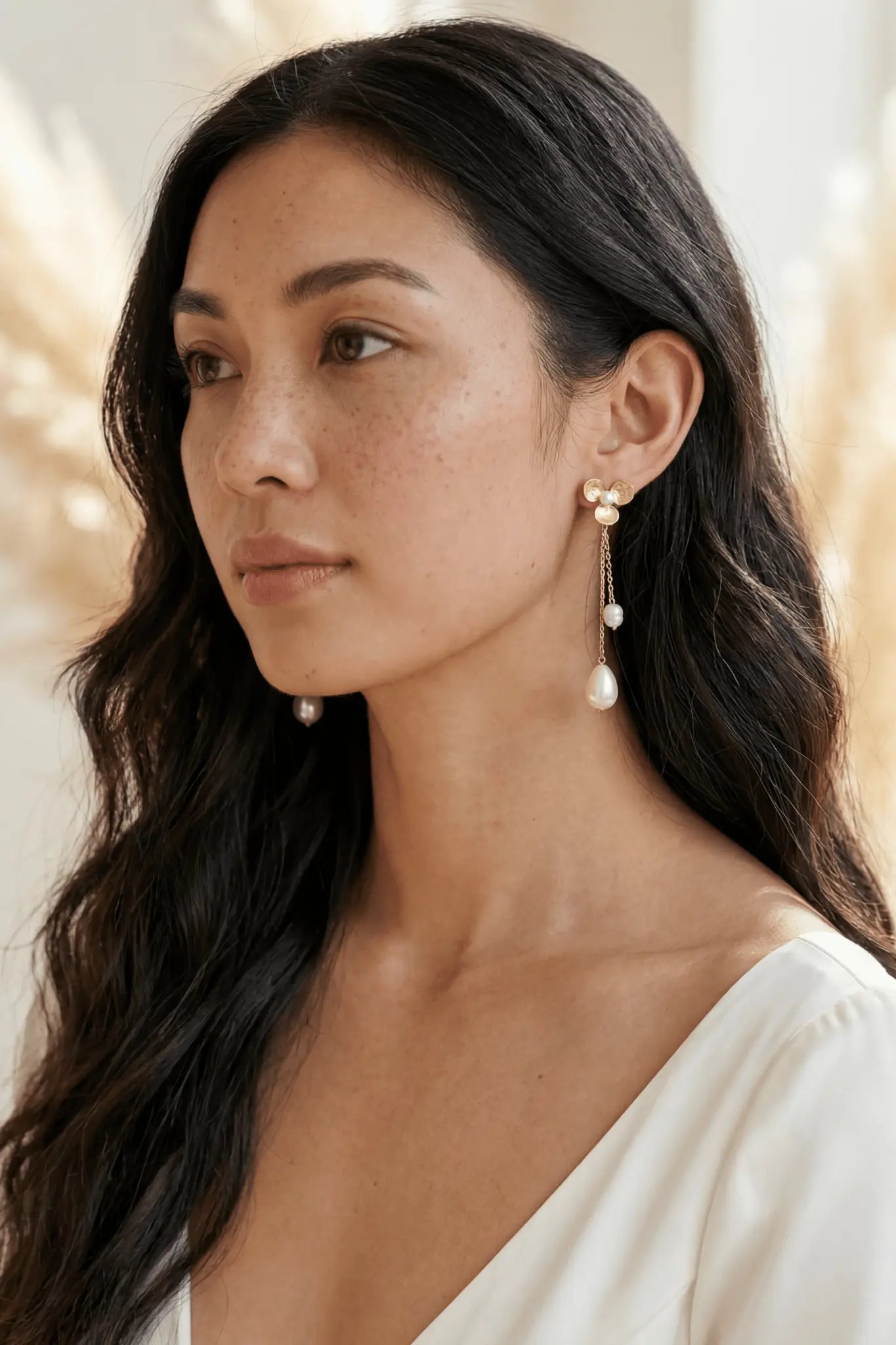 Filipino woman with long dark hair wearing floral designed fresh water pearl dangle earrings with a blurred background. Affordable bridal jewelry & Organic pearl jewelry handmade by Canadian jewelry maker