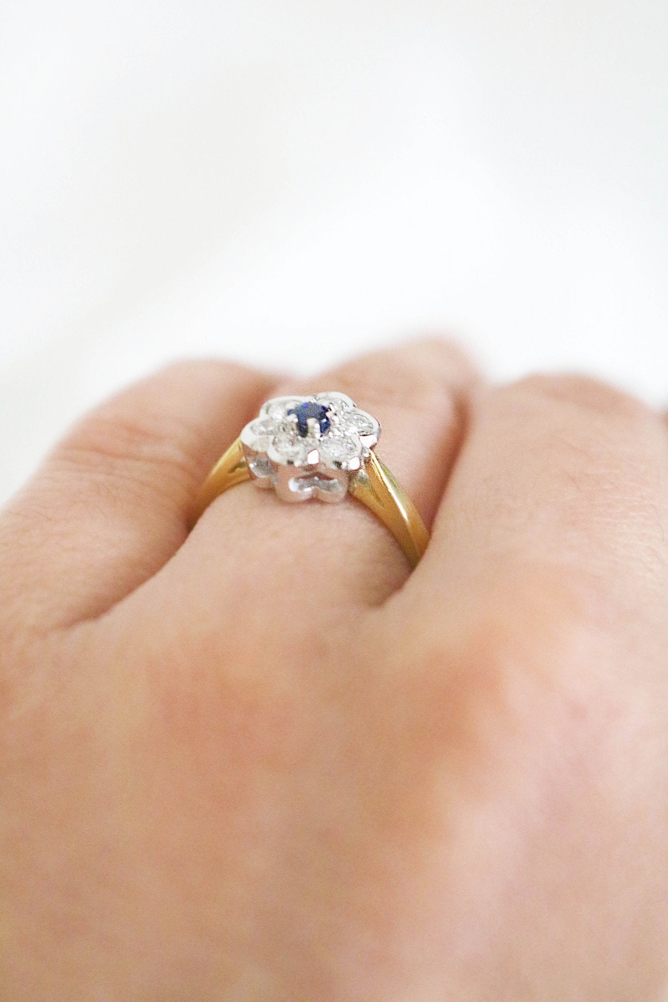 A white and yellow gold vintage engagement ring with a diamond and sapphire flower on a ring finger. Canadian vintage engagement rings. Bridal jewelry Canada. Canadian weddings. Wedding Canada. Canadian bridal jewelry. Woman-owned Canadian jewelry brand. Canadian jewelry brands.