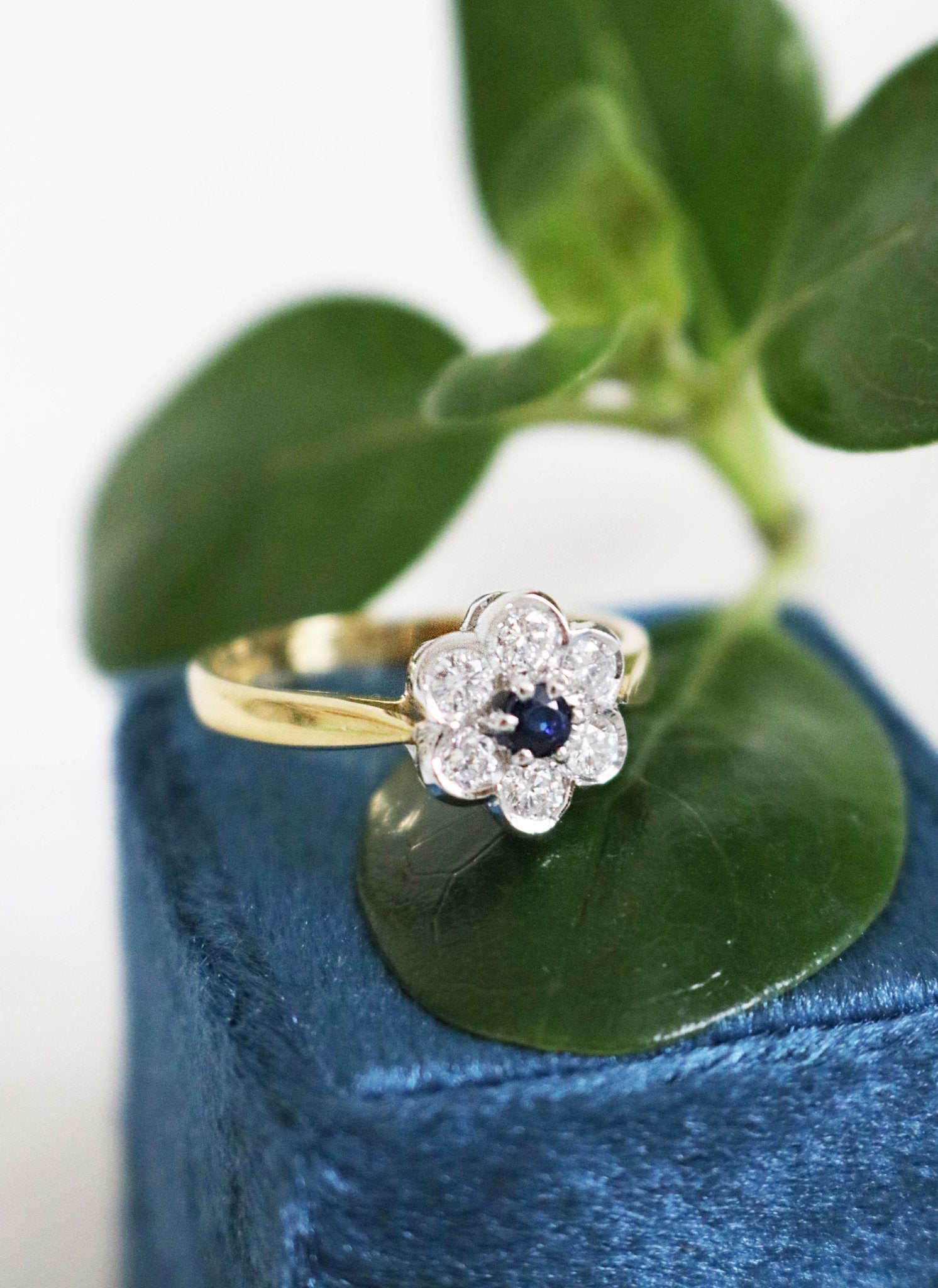 A close up of the 18ct white and yellow gold Florah Diamond  and sapphire Flower Vintage Engagement Ring sitting on a leaf on a ring box. Canadian vintage engagement rings. Bridal jewelry Canada. Canadian weddings. Wedding Canada. Canadian bridal jewelry. Woman-owned Canadian jewelry brand. Canadian jewelry brands.