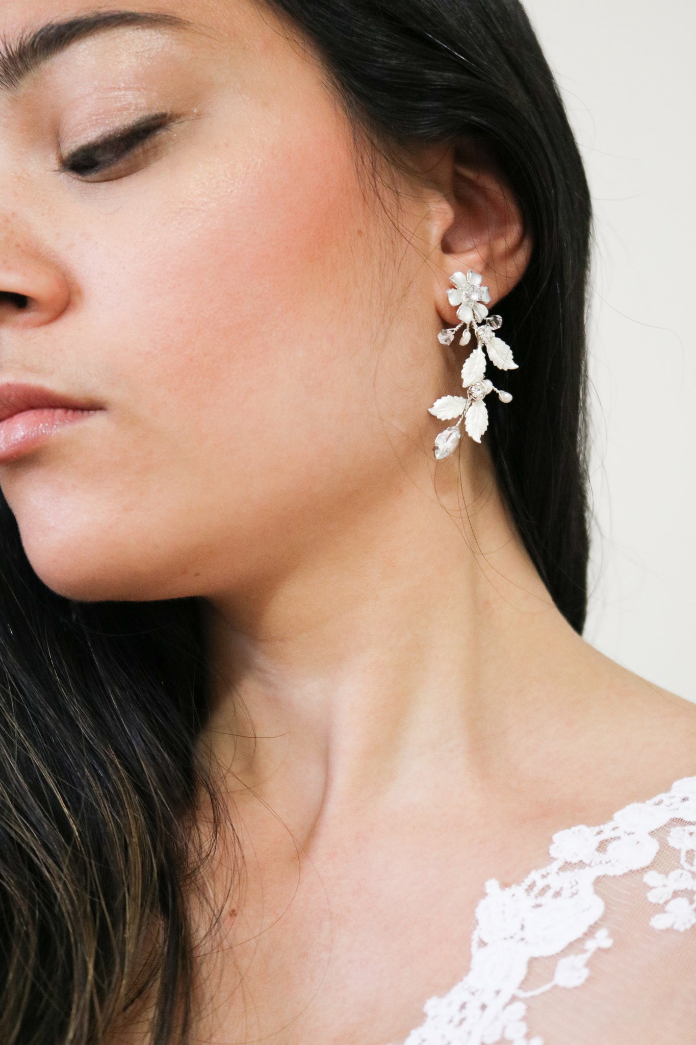 A close up of a bride wearing silver foliage dangle bridal earrings with crystals and leaves. 