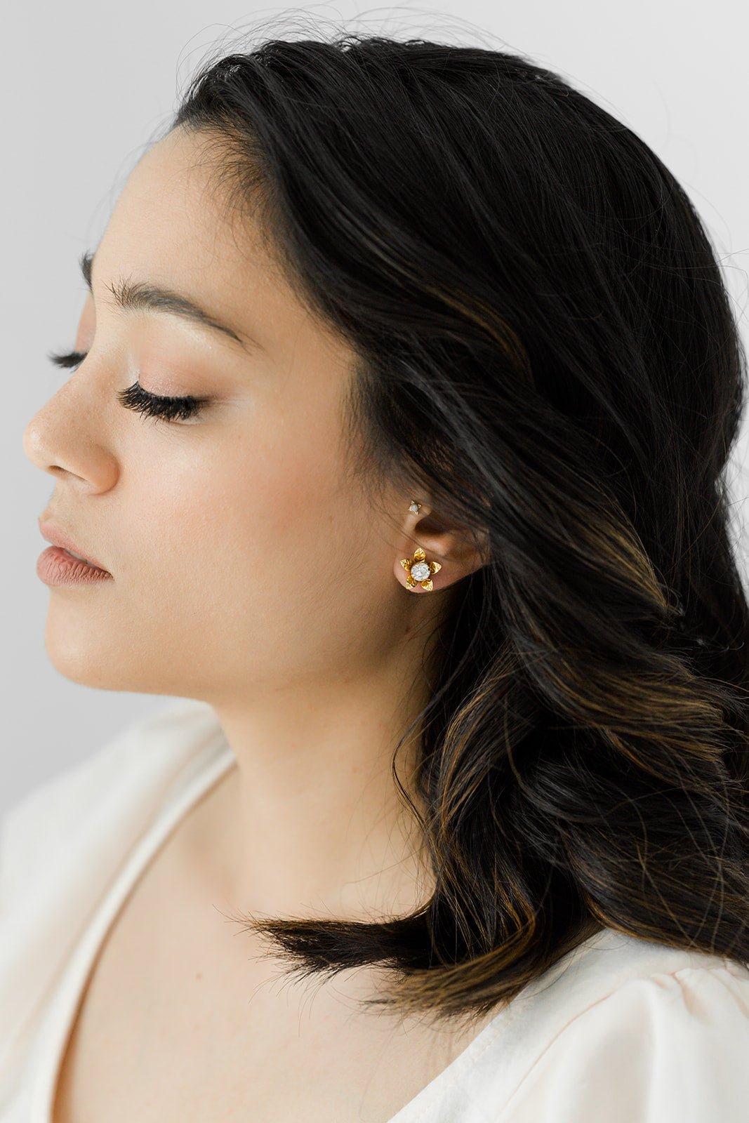 Woman with dark hair wearing gold flower bridal earrings with a neutral background. Bridal earrings & Handmade bridal jewelry by small Canadian jewelry brand