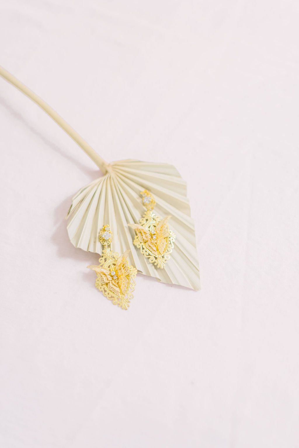 Flutura Gold Butterfly Earrings with Swarovski Crystals against a golden leaf. 