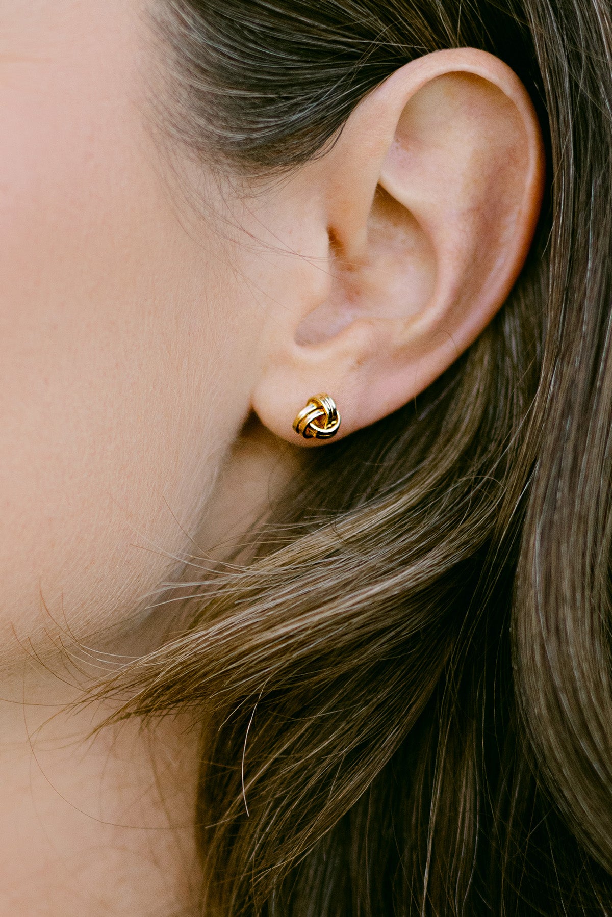 Close-up of an ear wearing a gold-filled knot earring. Minimalist Jewelry. Everyday jewelry. Woman-owned Canadian jewelry brand.