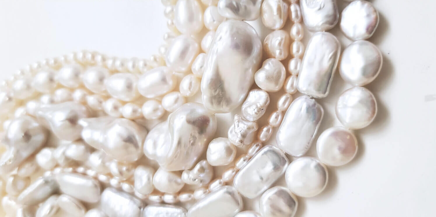 Several strings of freshwater pearls in various shapes on white background.
