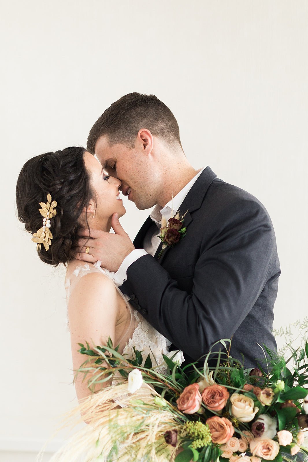 A happy bride and groom celebrate while her bridal do holds an elegant leafy golden hair comb with freshwater pearls. 