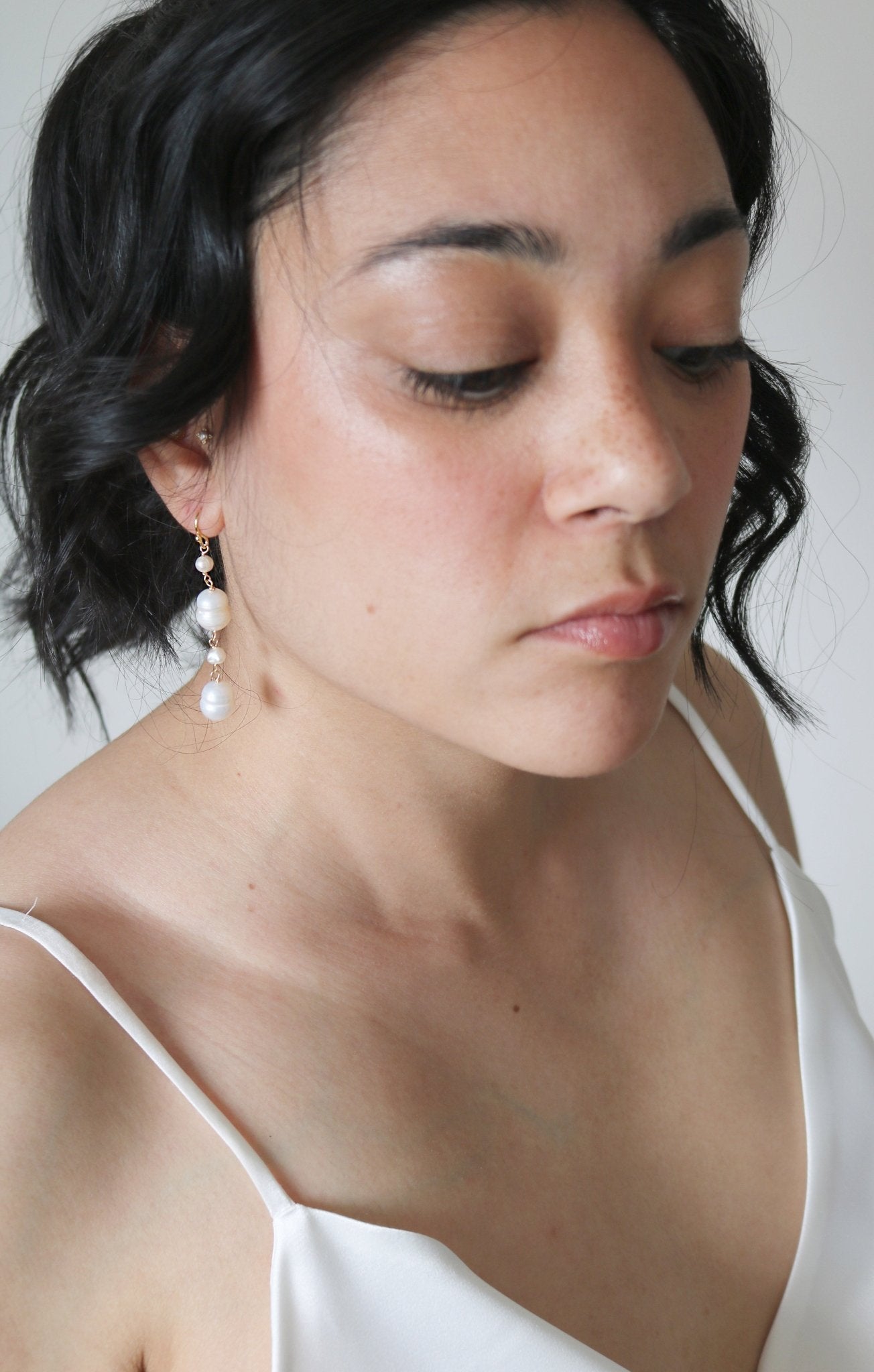 A thoughtful bride in a silky wedding gown showcases gold-filled drop down earrings with classy freshwater pearls. 