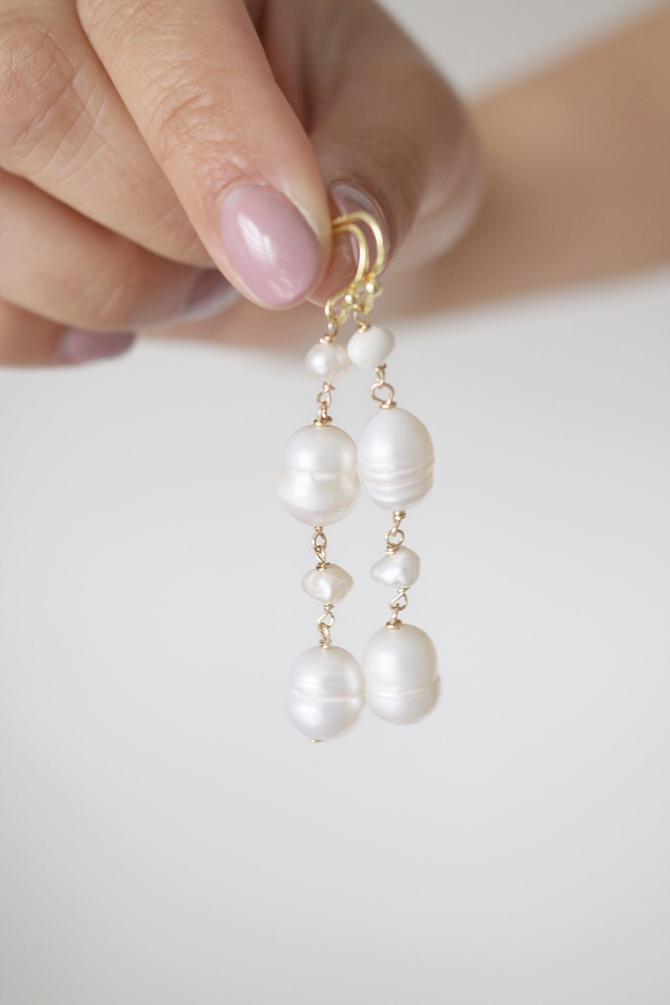 Fingers daintily hold freshwater pearl earrings with variously sized pearls. 