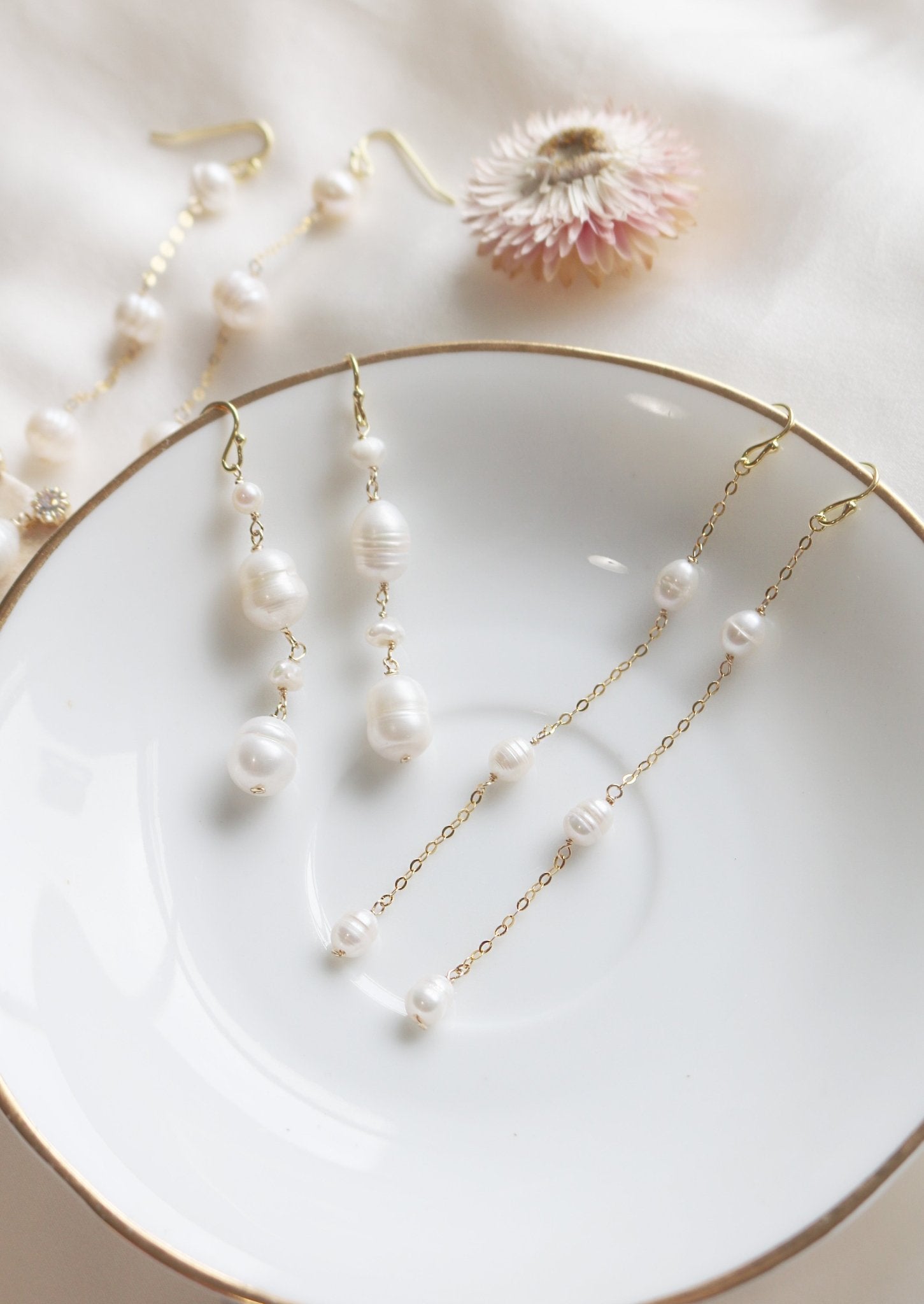 Two sets of gold-filled dangle earrings lay on a white plate, dripping with freshwater pearls. 