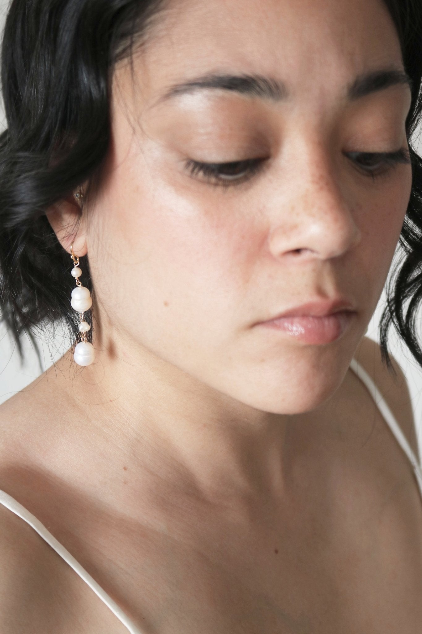 A thoughtful bride in a silky wedding gown showcases gold-filled drop down earrings with classy freshwater pearls. 