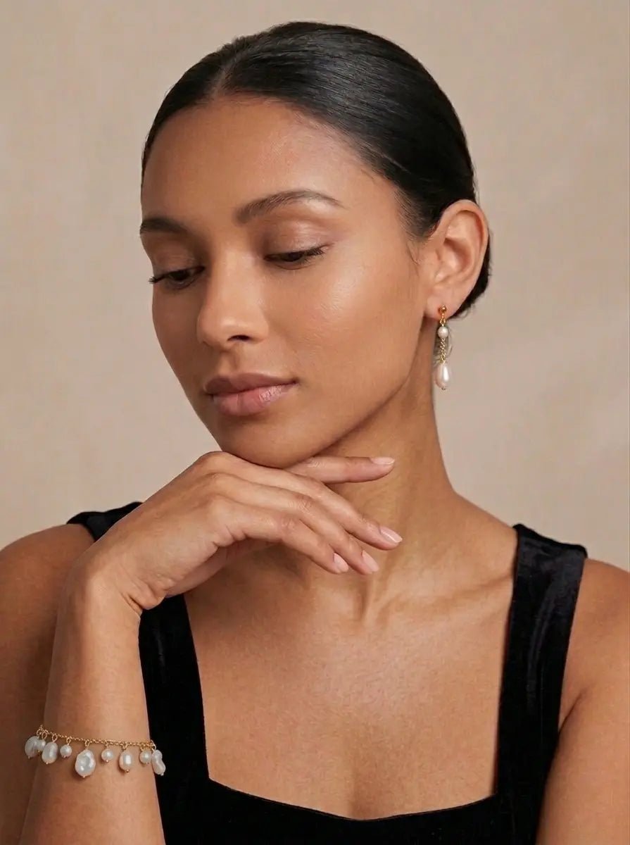 BIPOC woman wearing fresh water pearl drop earrings and pearl bracelet against a beige background. Pearl jewelry sets & Pearl jewelry Canada.