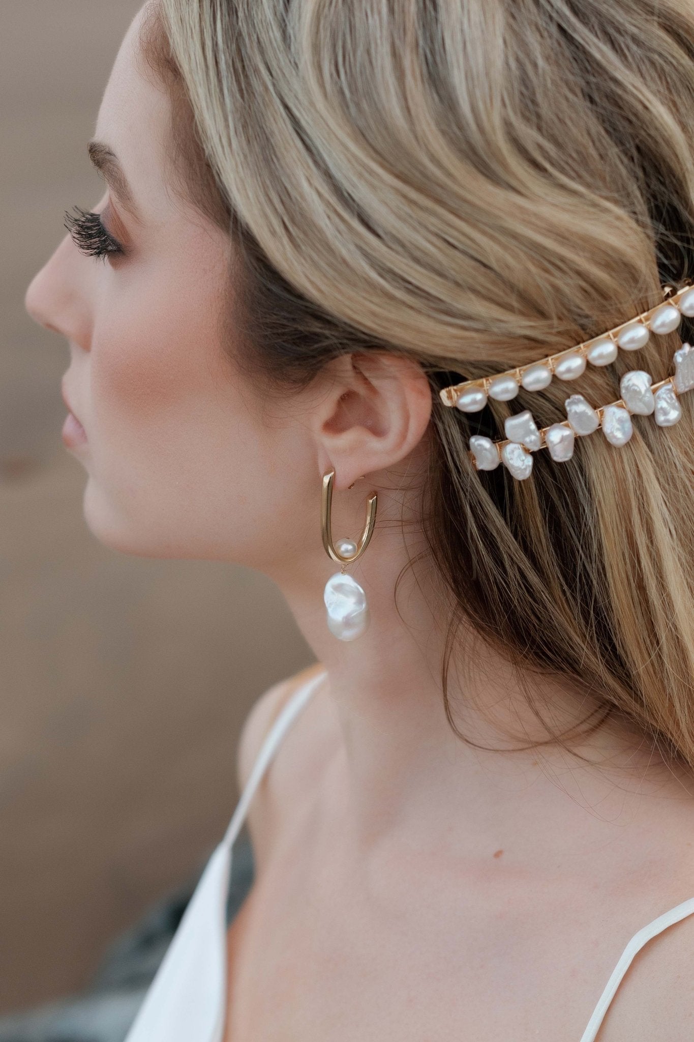 An elegant bride looks on while wearing small baroque freshwater pearl bridal earrings and gold pearl barrettes. 