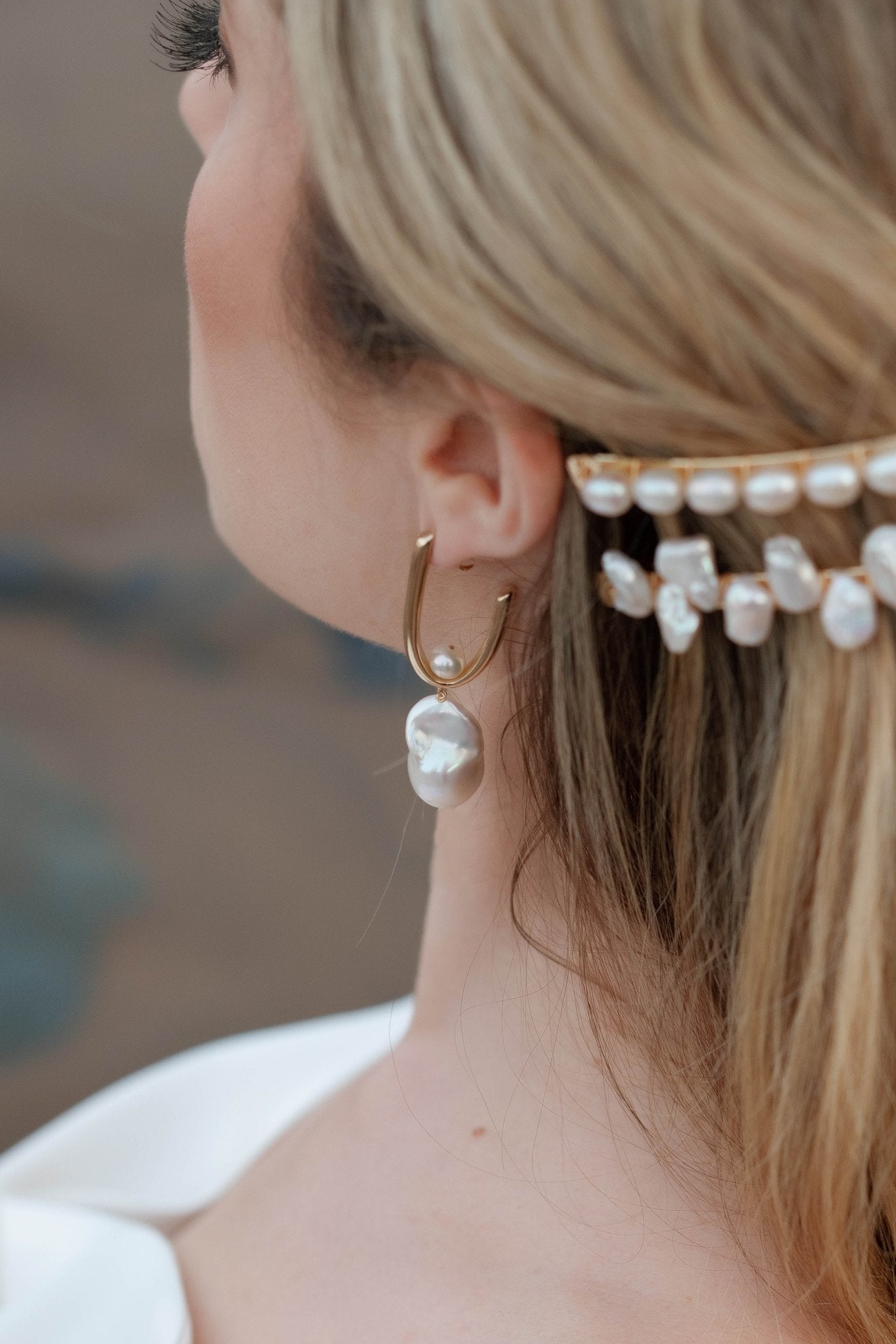 An elegant bride looks on while wearing small baroque freshwater pearl bridal earrings and gold pearl barrettes. 