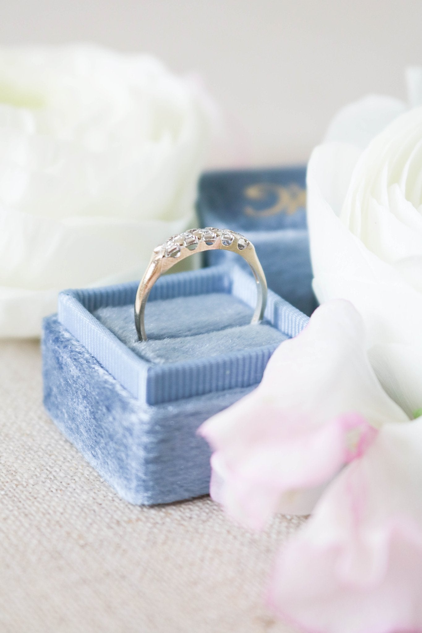 Side view of the Harmony Vintage Engagement Ring/Wedding Band in 14ct Gold with Diamonds in a ring box surrounded by white roses. 