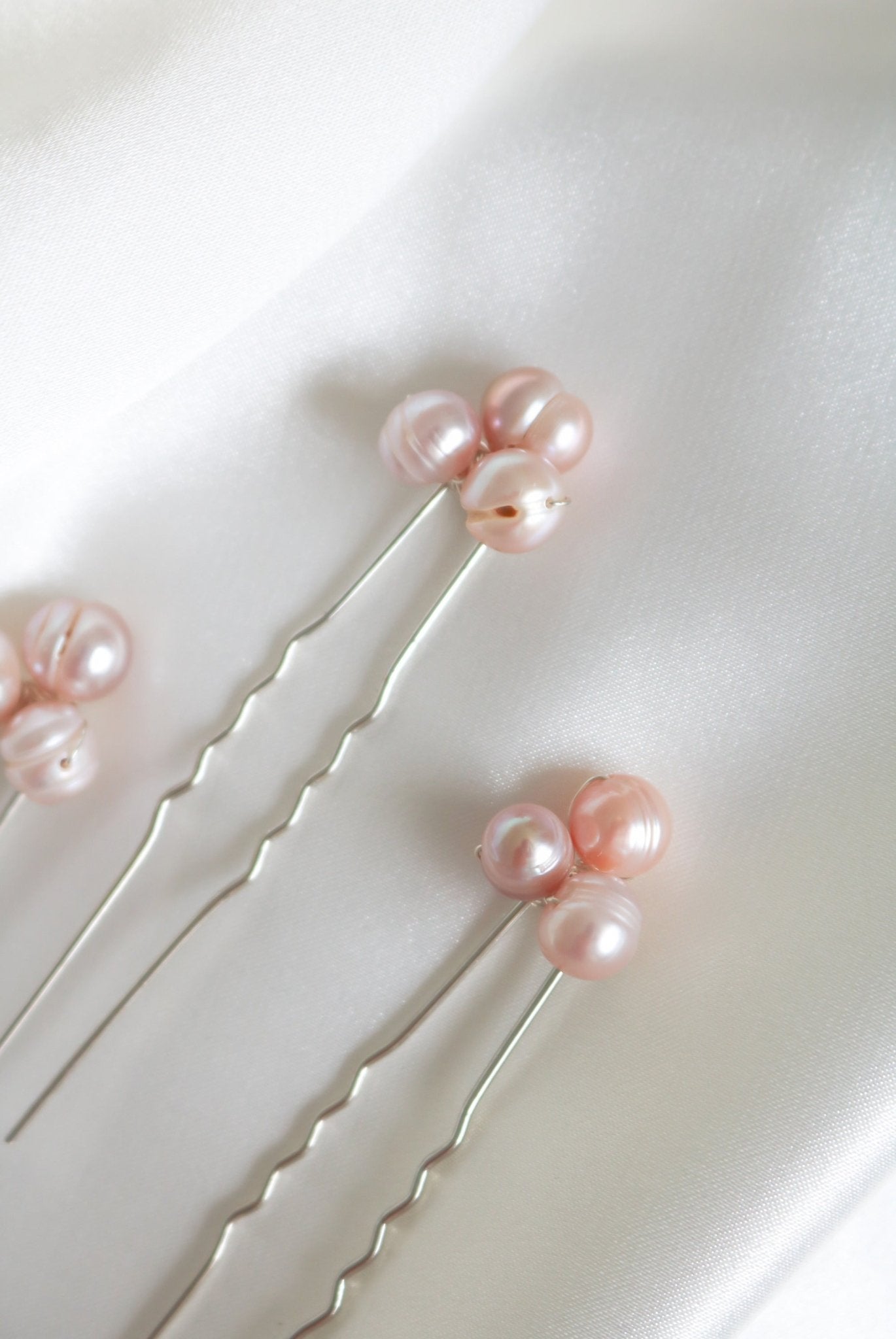 A close up of three silver freshwater blush pearl bridal hairpins on a white fabric background. Handmade bridal hair accessories & pearl bridal accessories by Canadian BIPOC jewelry designer