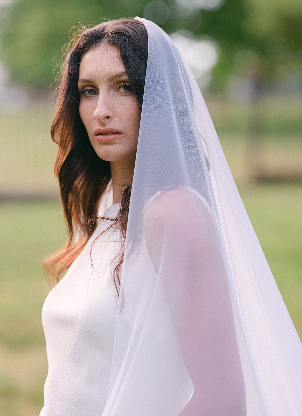 Bride looks down camera with full wedding veil draping down her back.