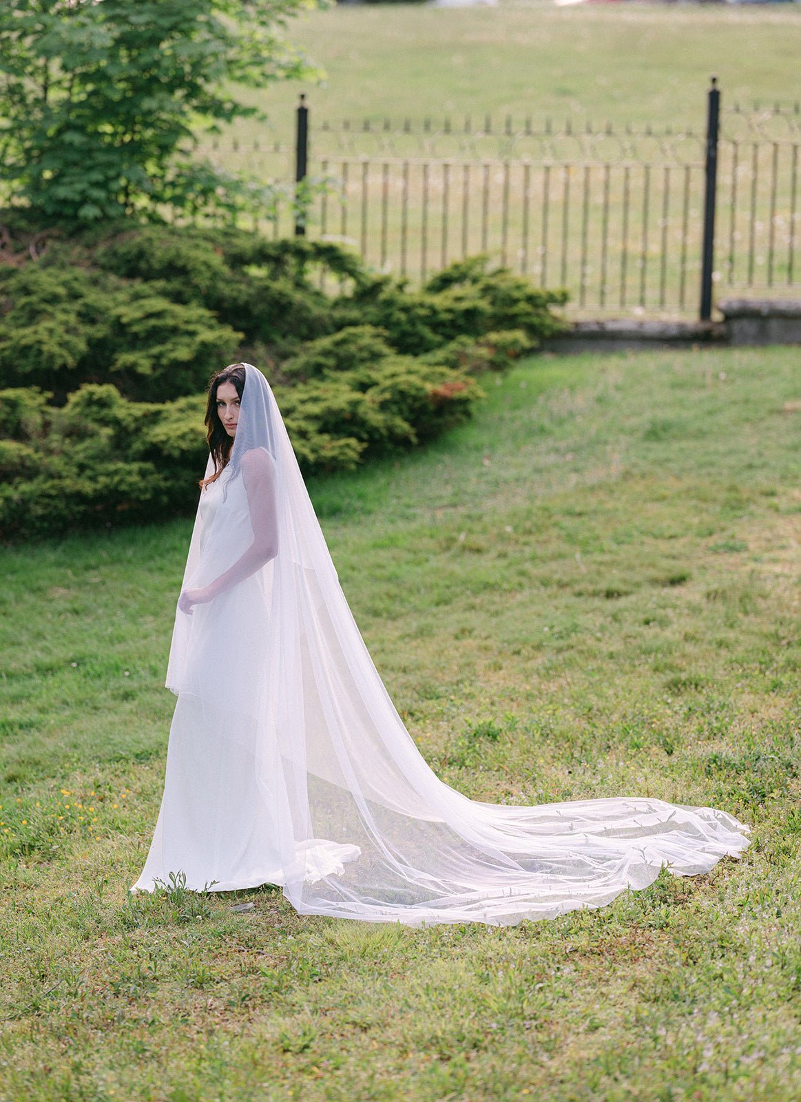 Long shot of bride and full white flowing wedding veil on a grassy lawn.