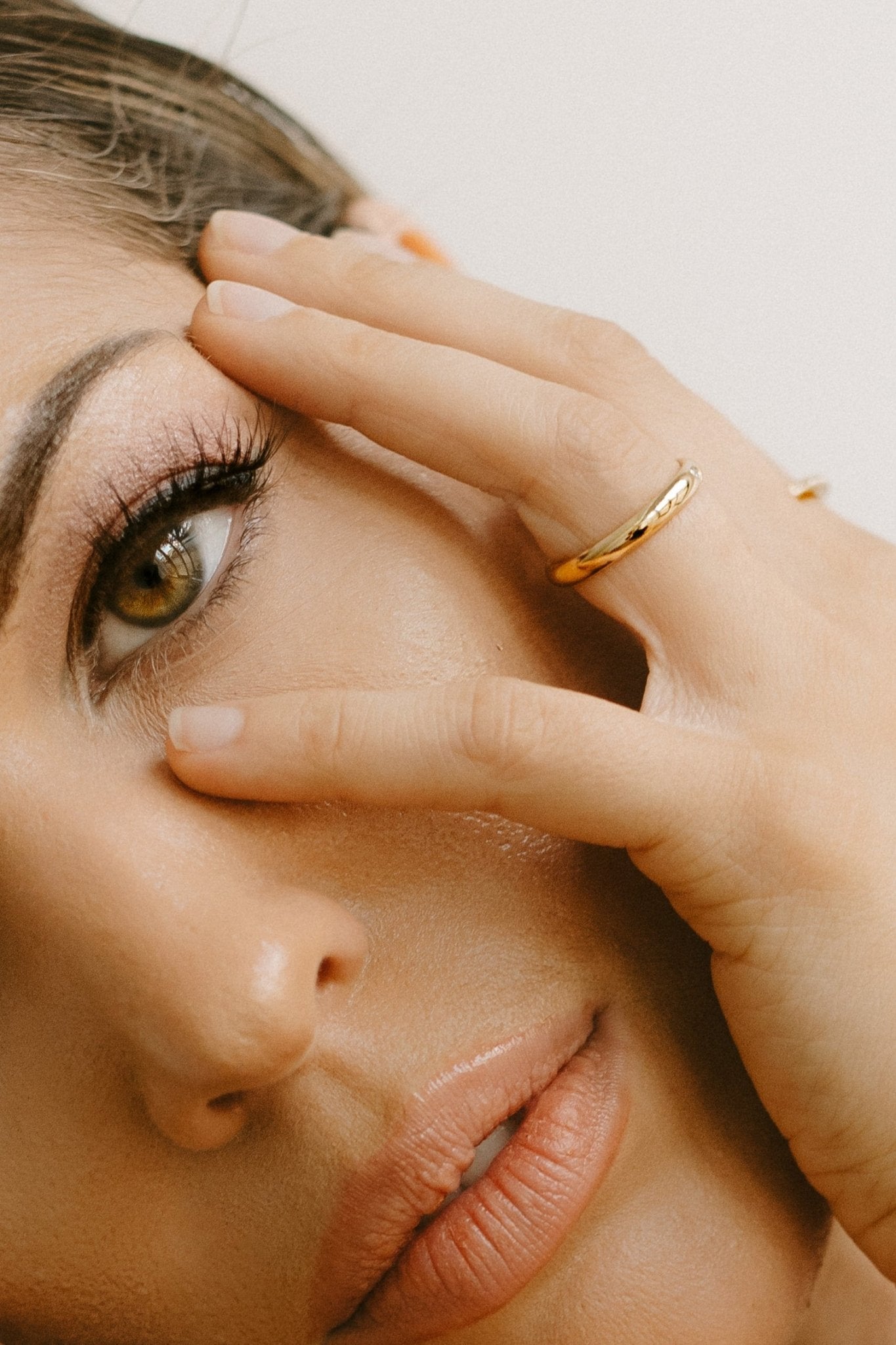 Close-up of a woman's face with one hand covering her eye, wearing a gold-filled band. Gold-filled Canadian jewelry. Small Canadian jewelry brands.
