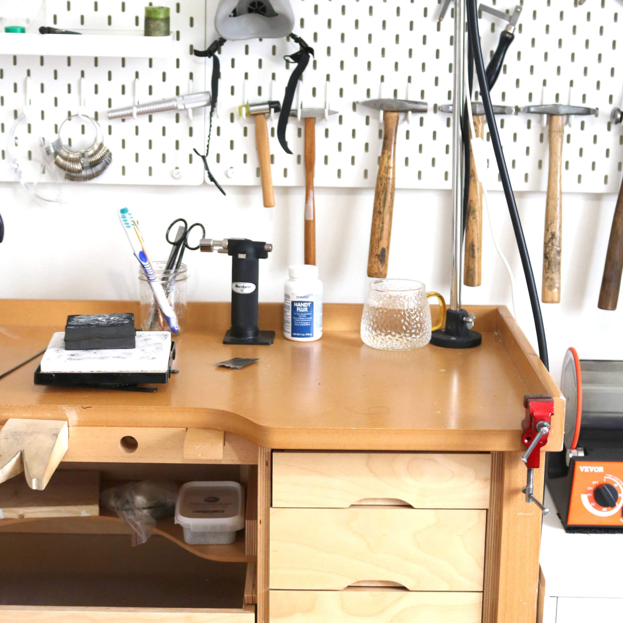 A wooden jewelry making bench with jewelry making tools hanging from the wall