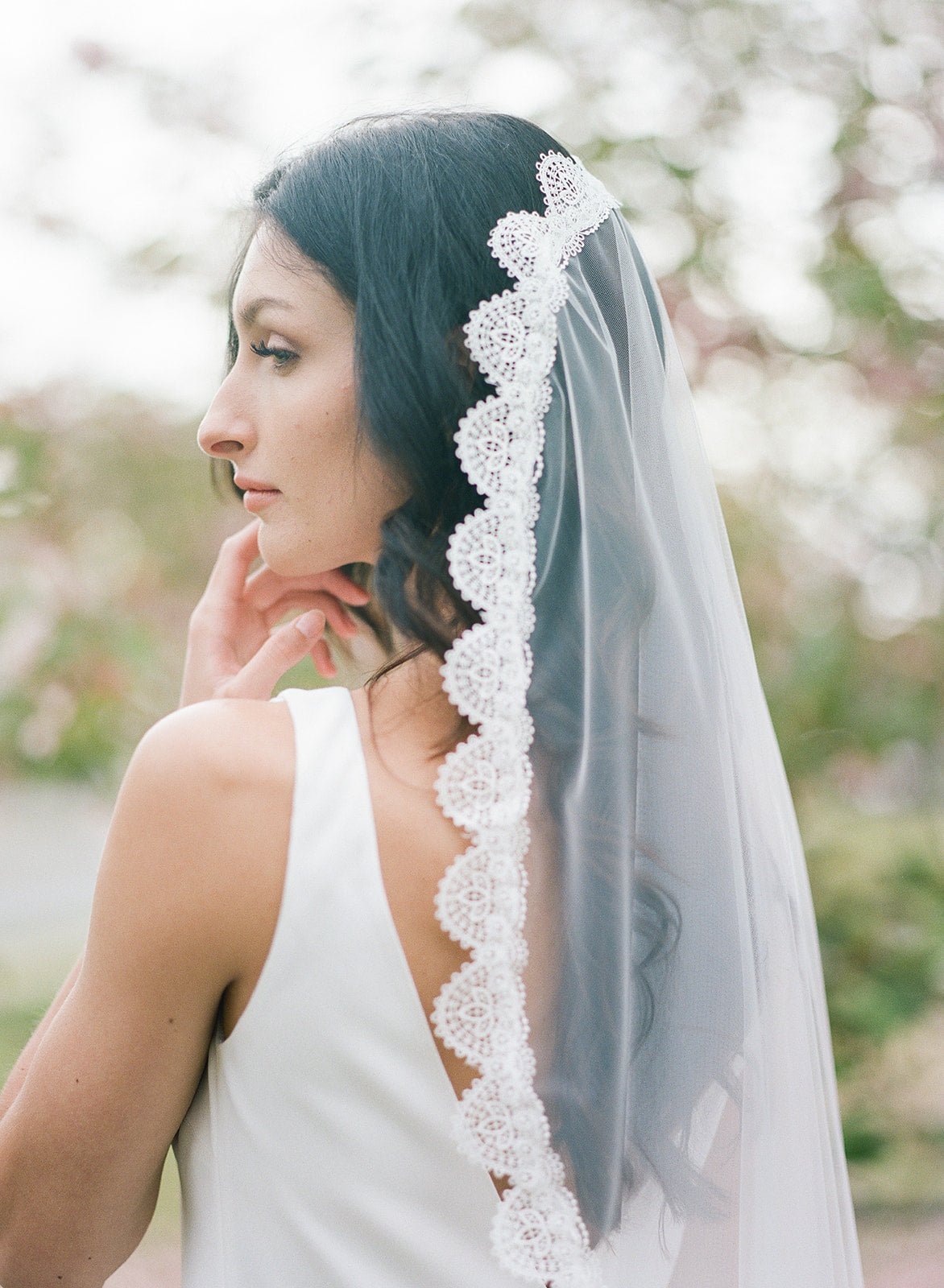 A bride in white looking over her shoulder wearing a wedding dress with a sheer lace veil.