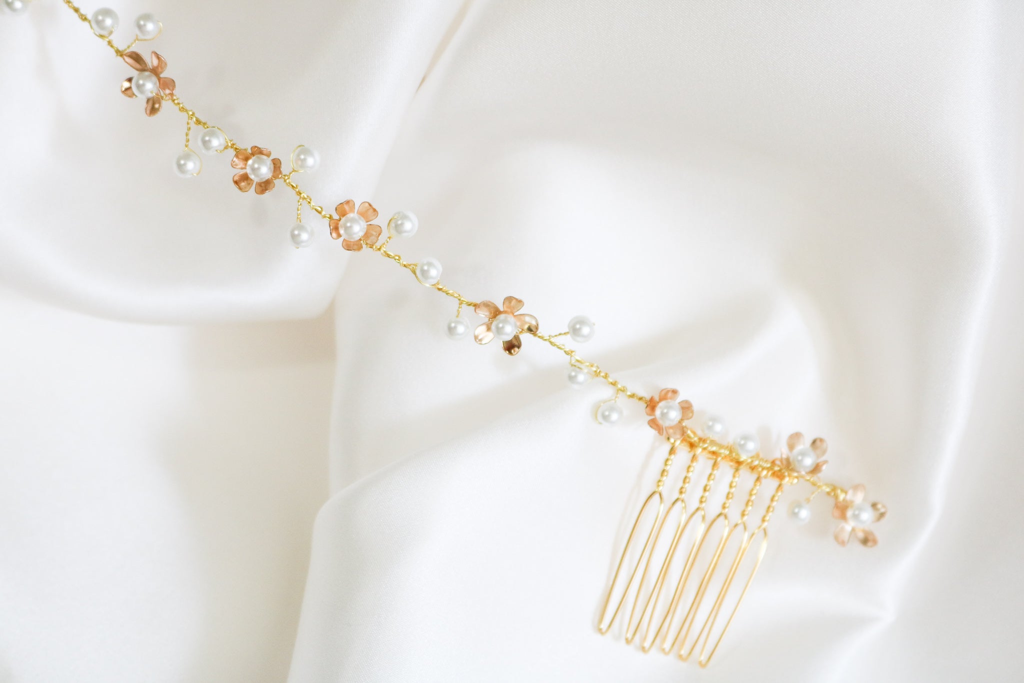 A close up detailed look at the gold Juliette freshwater pearl floral bridal hairvine against a white satin sheet. 