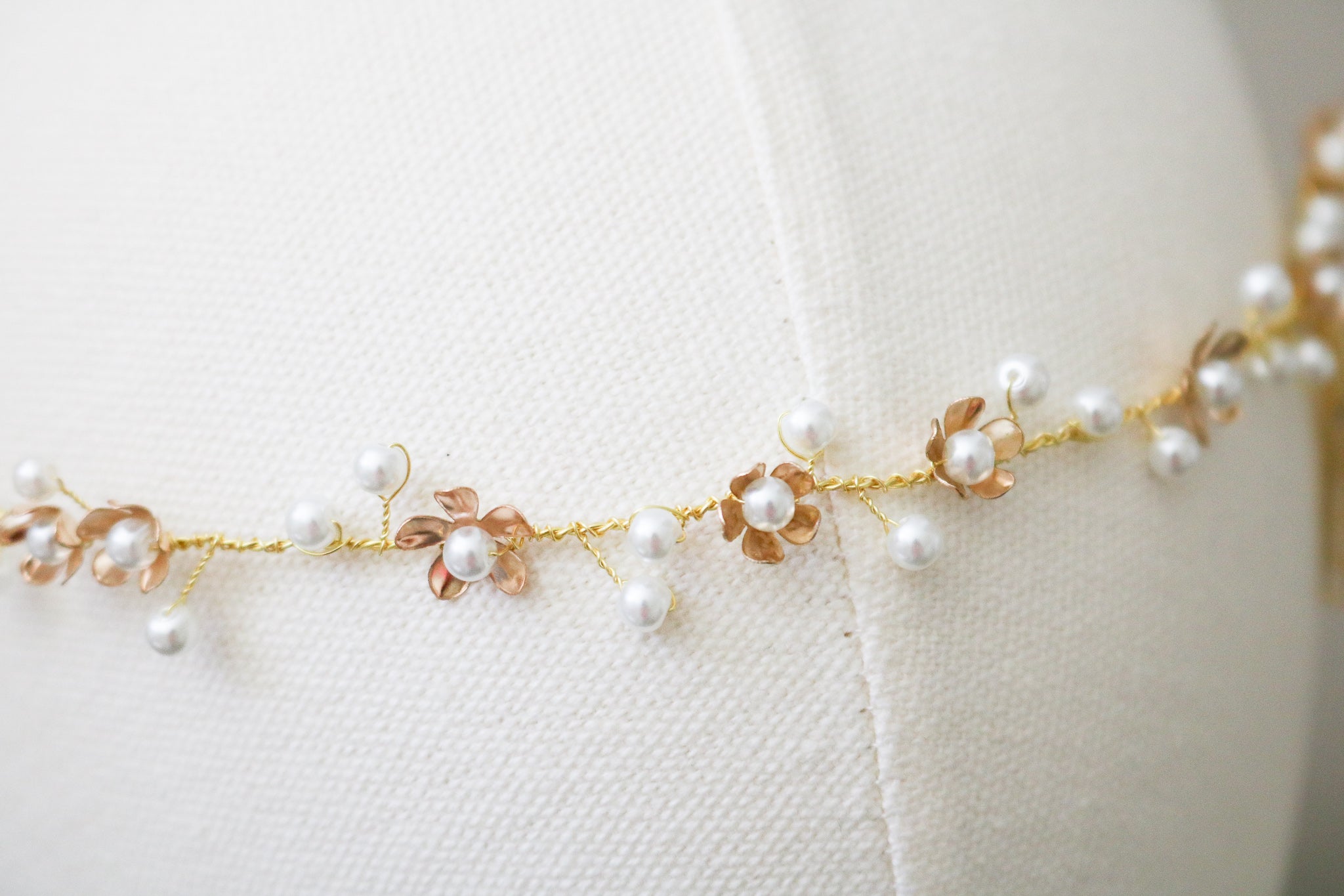 An extreme close up of a gold bridal hairvine with freshwater pearls displayed on a head bust. 