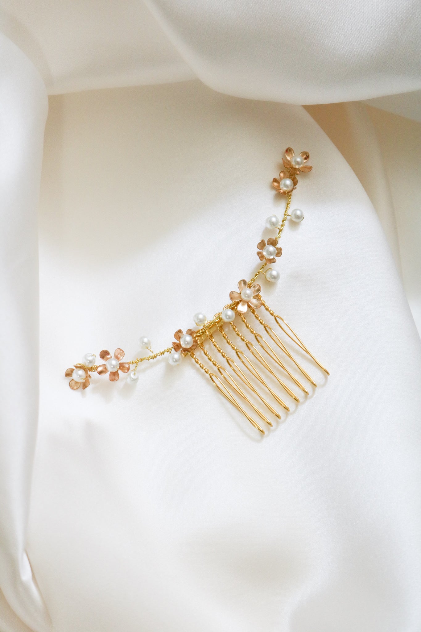 A Gold floral bridal hair comb with freshwater pearls is nestled between sheets of white satin. 