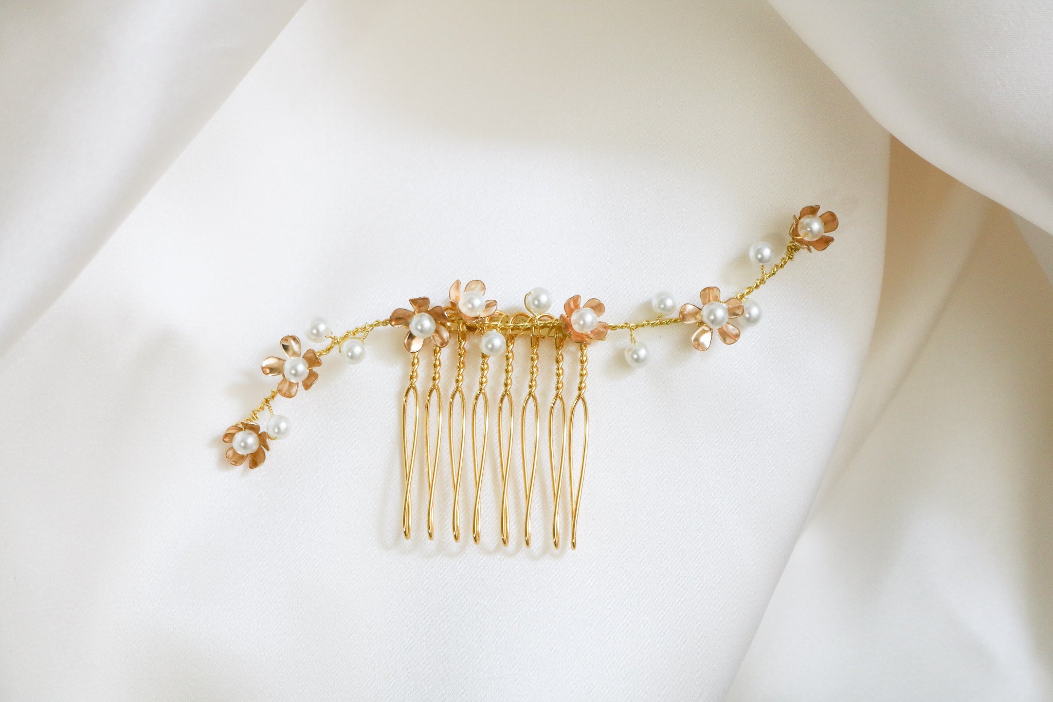 A close up of a gold bridal hair comb with freshwater pearls sitting on a white satin background. 