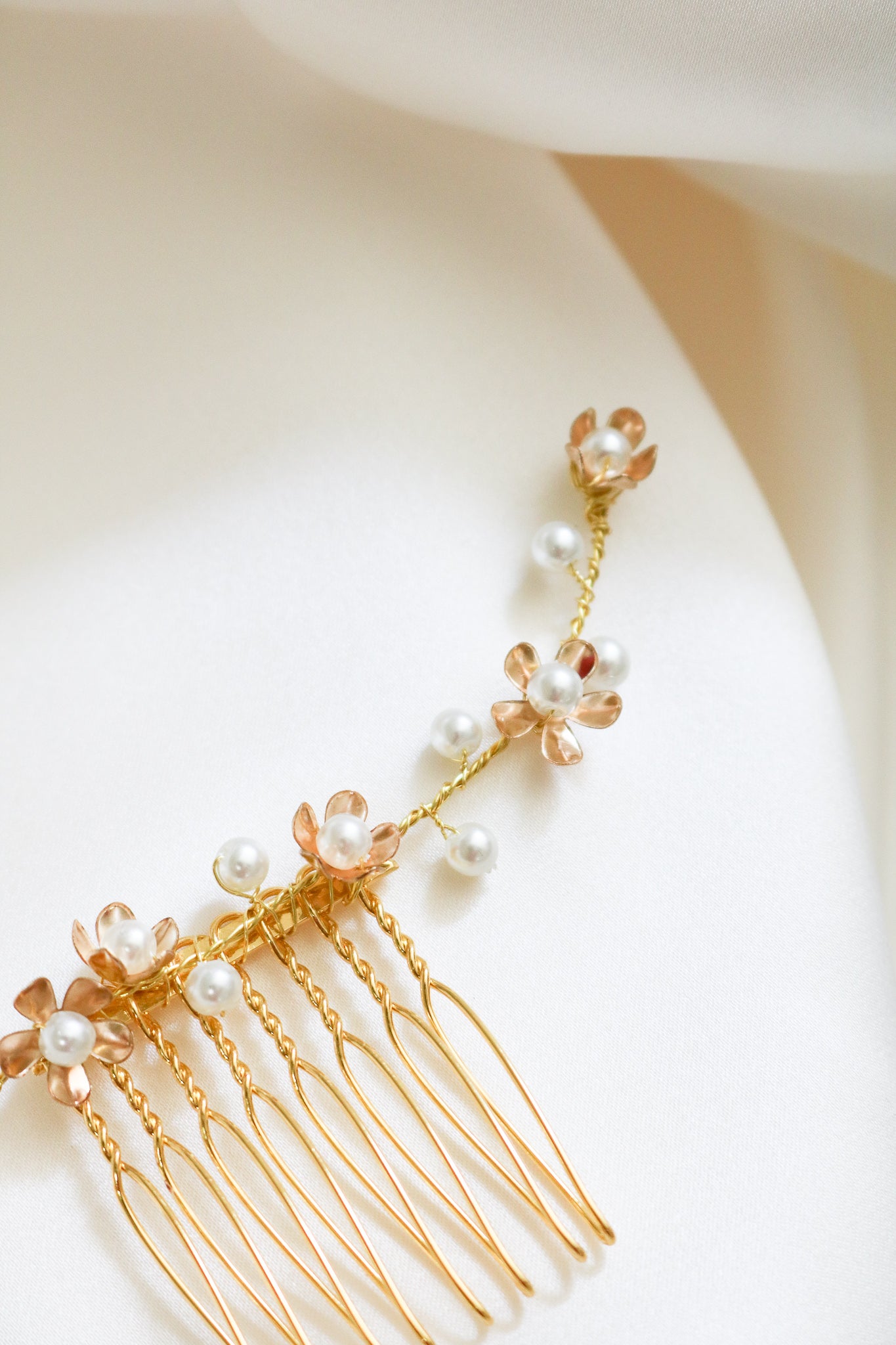 An extreme close up of a shorter gold freshwater pearl floral bridal hair comb displayed on the side of a mannequin head.