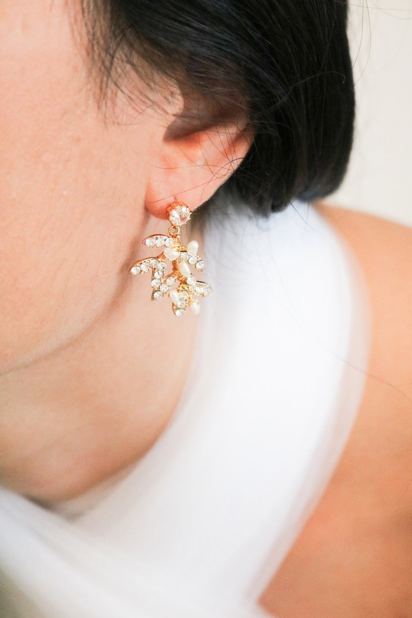 A gold-filled crystal leaf and freshwater pearl stud hangs from a woman's ear. 