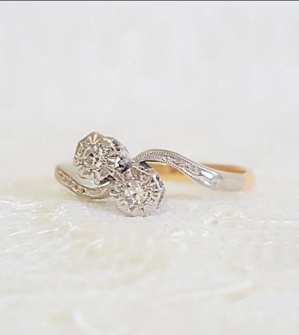 A close up of a diamond, 18k gold vintage engagement ring with platinum on a glossy white display.