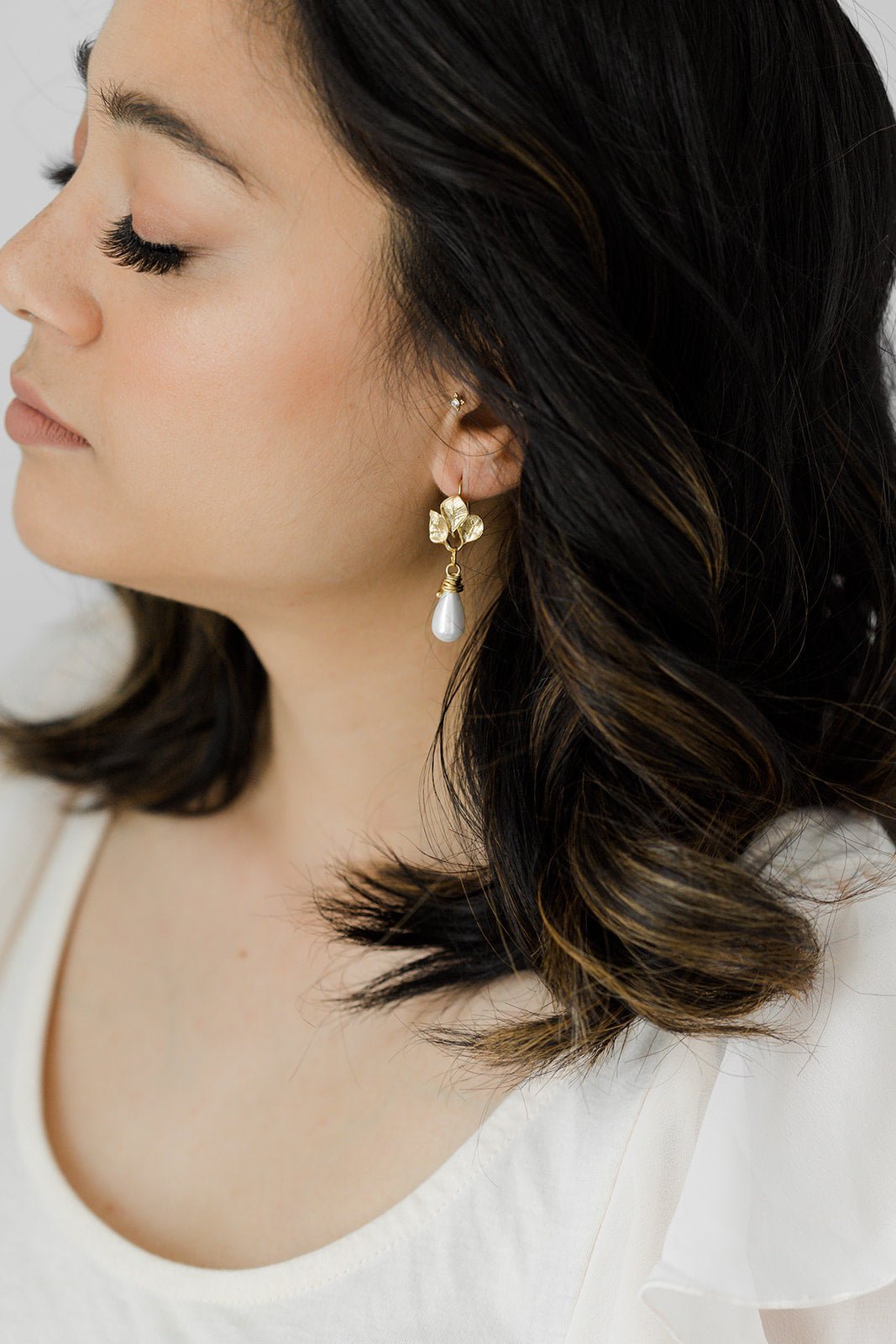 A pair of Gold-Filled Lily Drop Freshwater Pearl Leaf Earrings hanging from a woman's ear.