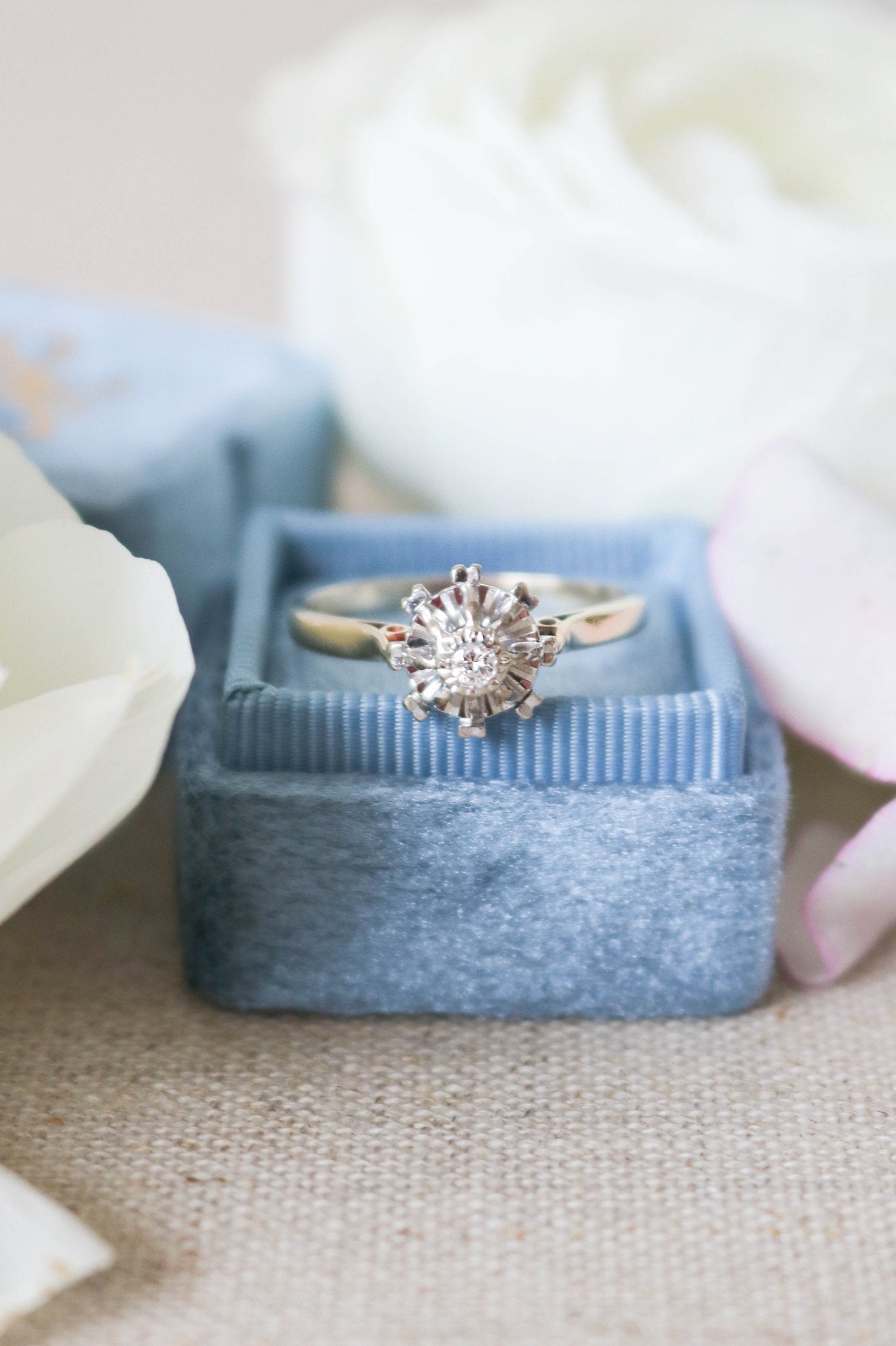 The Liona Floral Engagement Ring in 14ct Gold, Art Deco 1920s sits on top of a blue ring box surrounded by white roses. Antique Engagement Rings Canada. Canadian vintage engagement rings. Vintage engagement rings Canada. Bridal jewelry Canada. 