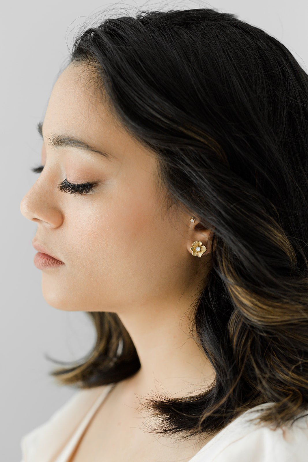 A woman with short dark hair wearing a gold flower earring with crystal against white background. Handmade Canadian jewelry, Minimalist bridal jewelry, & Gold-filled jewelry Canada