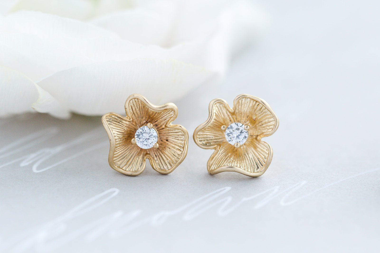 A close up of a pair of gold-filled flower studs with cubic zirconia crystals and sterling silver posts on a blurred background. Bridal jewelry Canada. Pearl jewelry Canada. Pearl Bridal jewelry Canada. Gold-filled jewelry Canada. Gold-filled Canadian jewelry. Handmade Canadian jewelry. Canadian handmade jewelry. Small Canadian jewelry brands. Canadian jewelry brands.