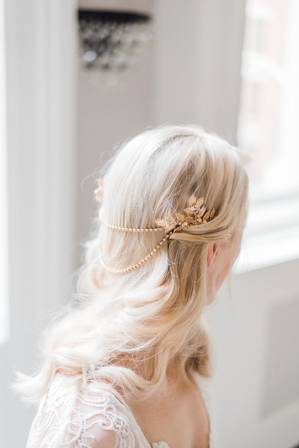 A blonde-haired bride in white lace looks away. A gold and crystal draped hairpiece and bridal hair accessory tucked in her hair. Bridal Hair Accessories & handmade Canadian accessories by BIPOC bridal jewelry designer