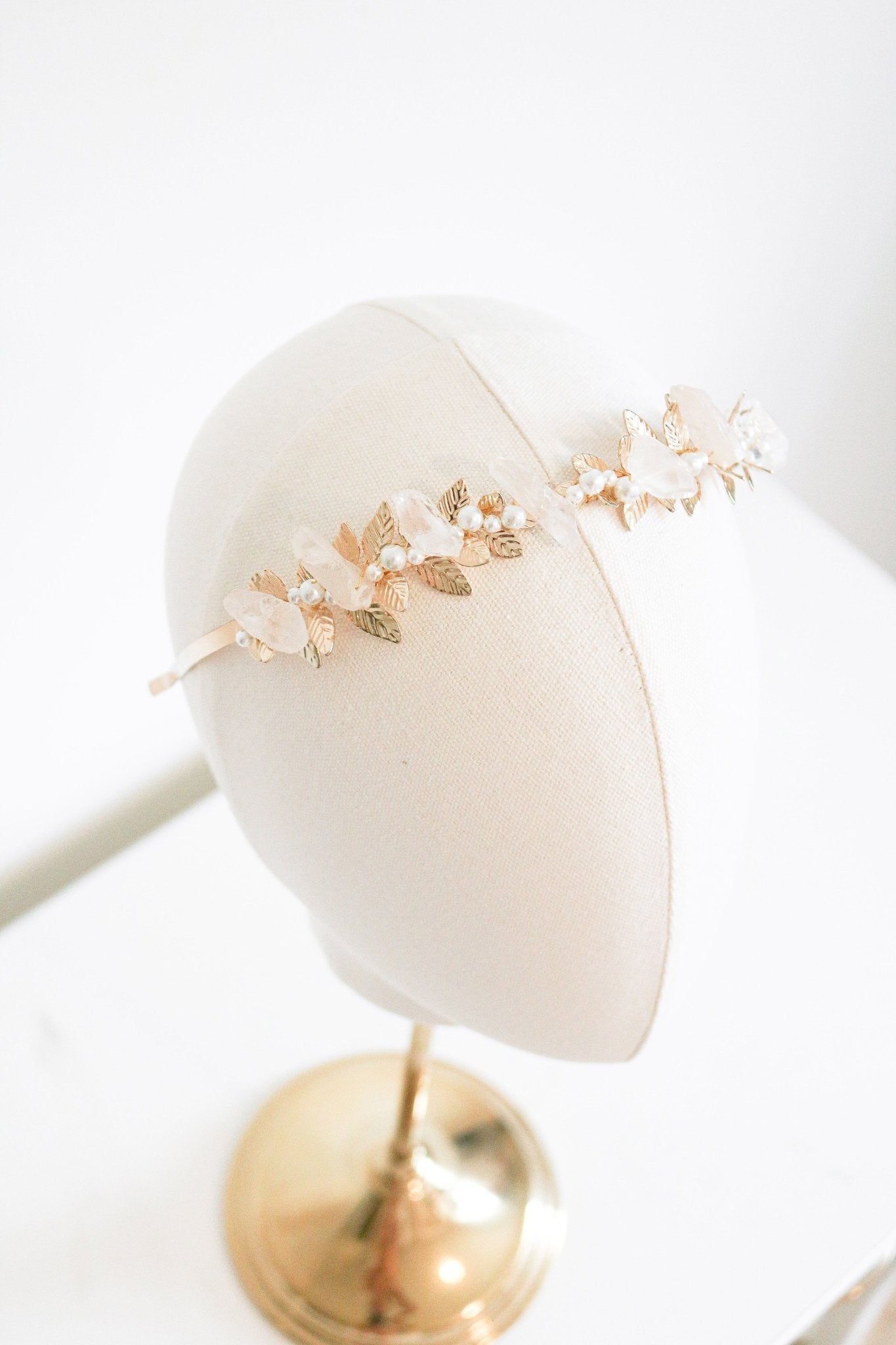 A gold laurel bridal headband with quartz crystals and freshwater pearls displayed on a head bust. Bridal hair accessories & handmade bridal accessories by BIPOC bridal jewelry designer