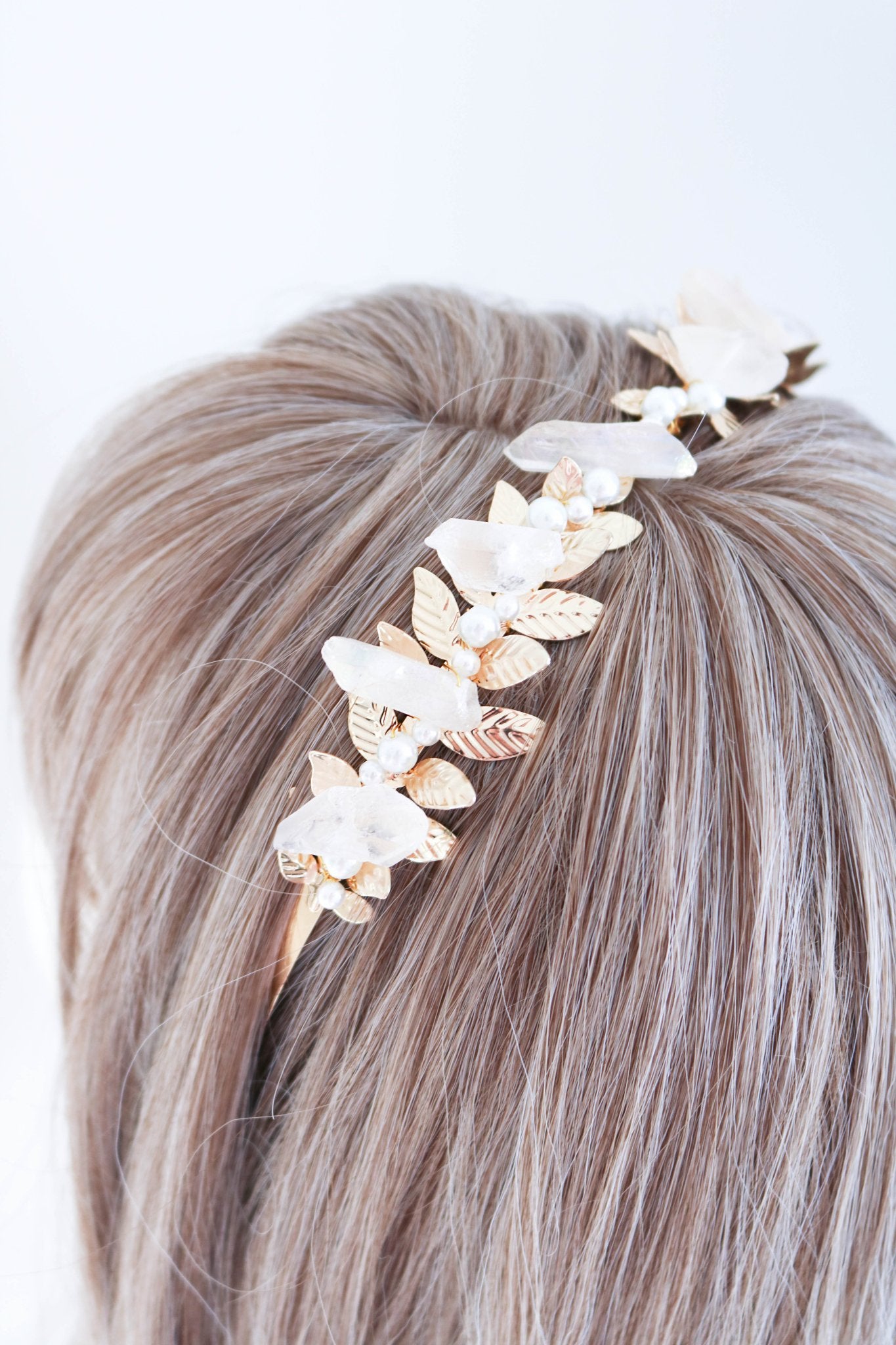 Close up top view of a gold laurel bridal headband with pearls and quartz crystals on a blonde wig with white background. Bridal hair accessories & handmade bridal accessories by BIPOC bridal jewelry designer