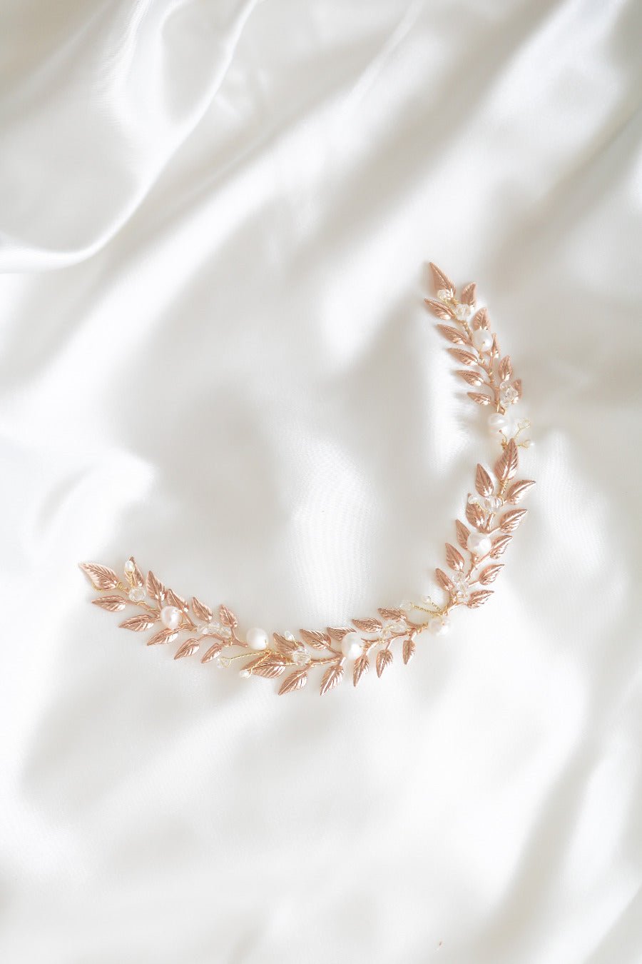 A top view of a gold Loriana Laurel Bridal Hairvine with Fresh Water Pearls sitting on a white satin sheet. Organic pearl accessories. Pearl Bridal Hair Accessories. Pearl Bridal Accessories. Bridal Hair Accessories. Bridal Accessories. Canadian Bridal Accessories. Handmade Canadian Accessories. Canadian handmade Accessories. Canadian weddings. Wedding Canada. 