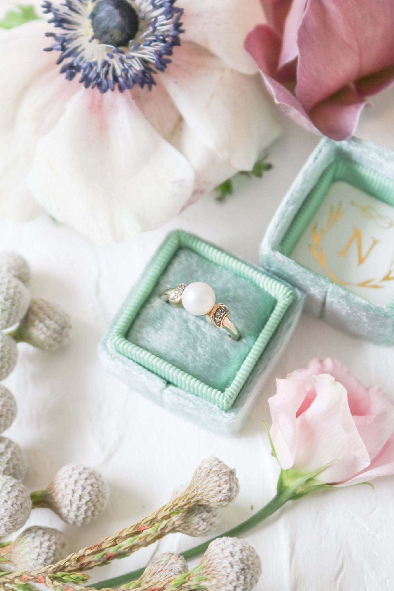 The Luna Diamond and Pearl Vintage Engagement Ring in 9ct Gold sitting in a seafoam green ring box. 