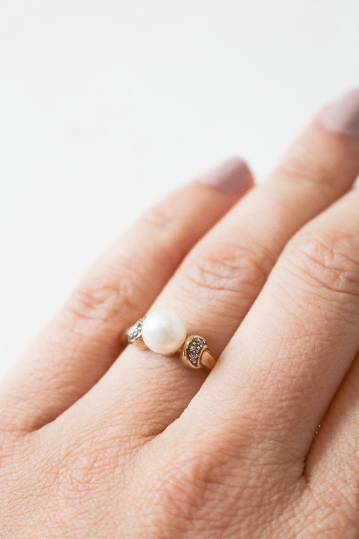 A gold and pearl vintage engagement ring with diamonds on a ring finger.