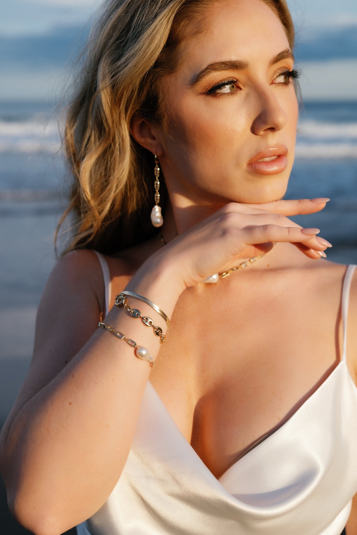 A beautiful bride on the beach shows off her bracelet stack and matching set of crystal with baroque pearl earrings and bracelet. 