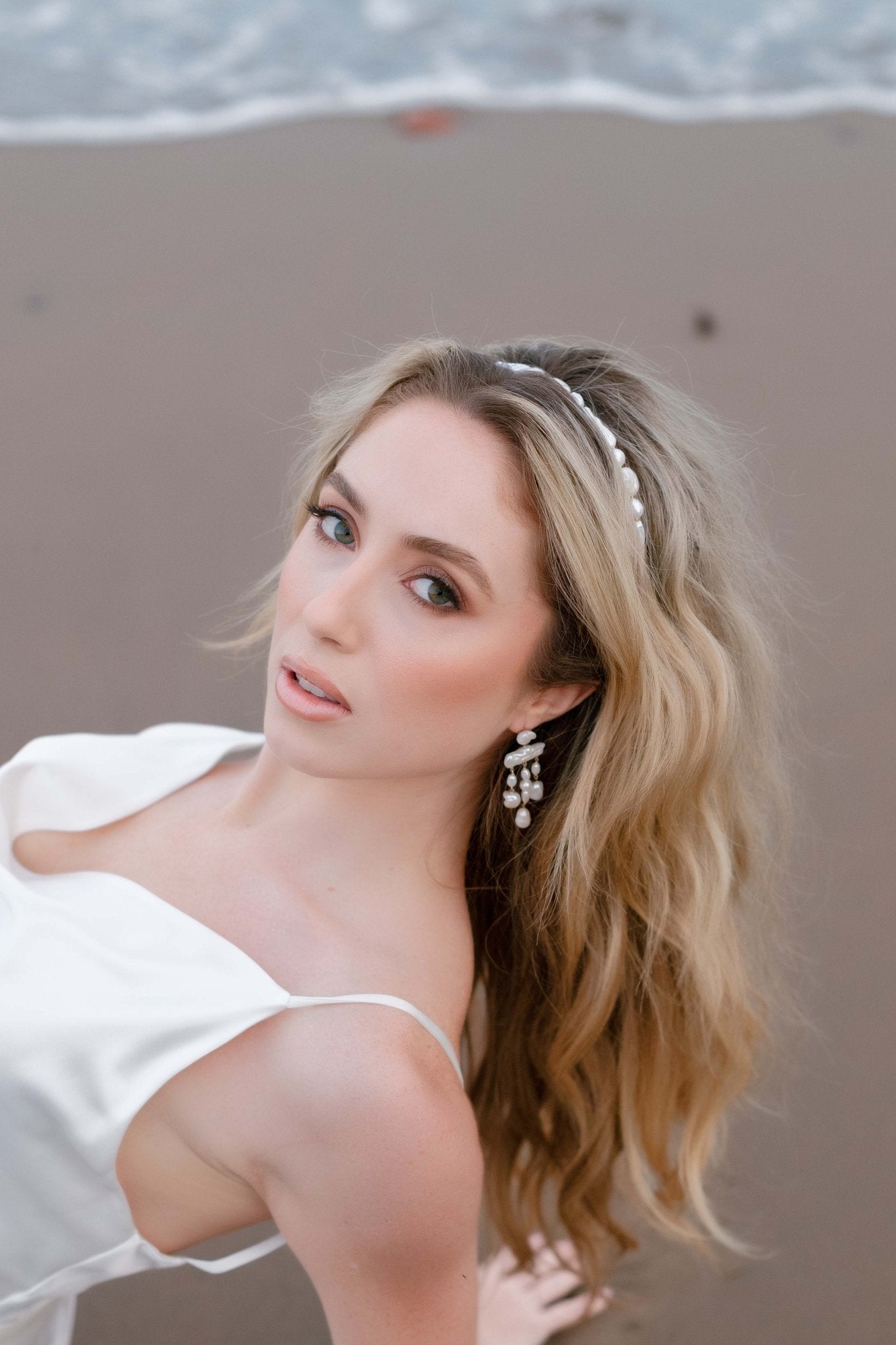 Bride on beach sand in a satin wedding gown accessorizes with freshwater pearl headband and earring set. 